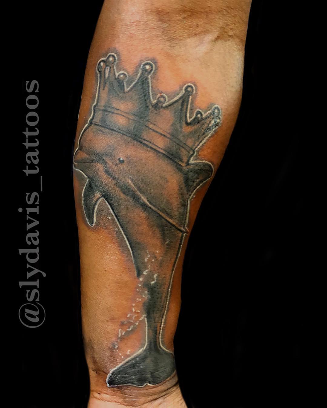 Dolphin wearing crown realism tattoo on the forearm by Sly Davis
