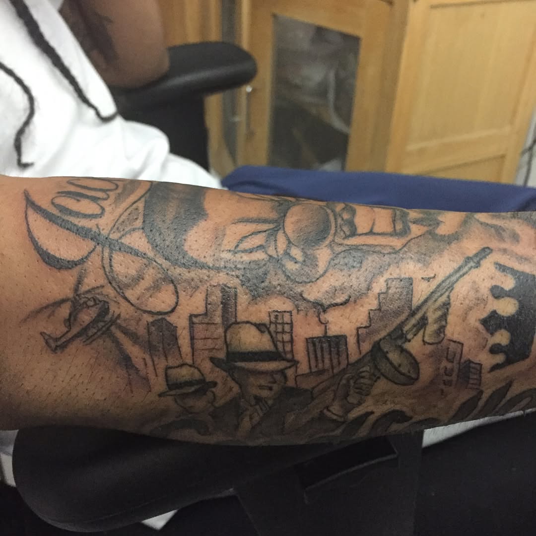 Cityscape with figures black and grey tattoo on the forearm by Junior Trevino