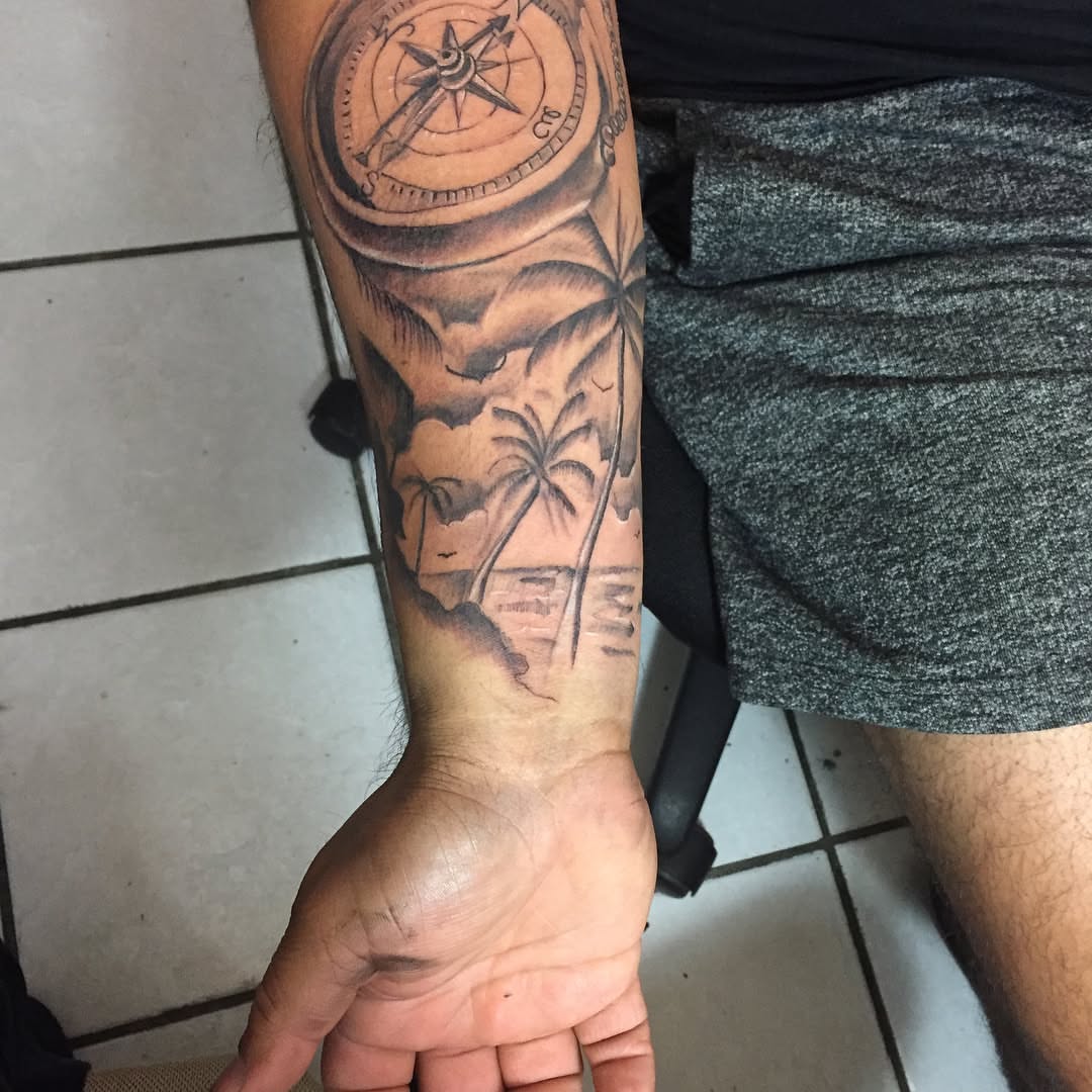 Compass and palm trees black and grey tattoo on the forearm by Junior Trevino