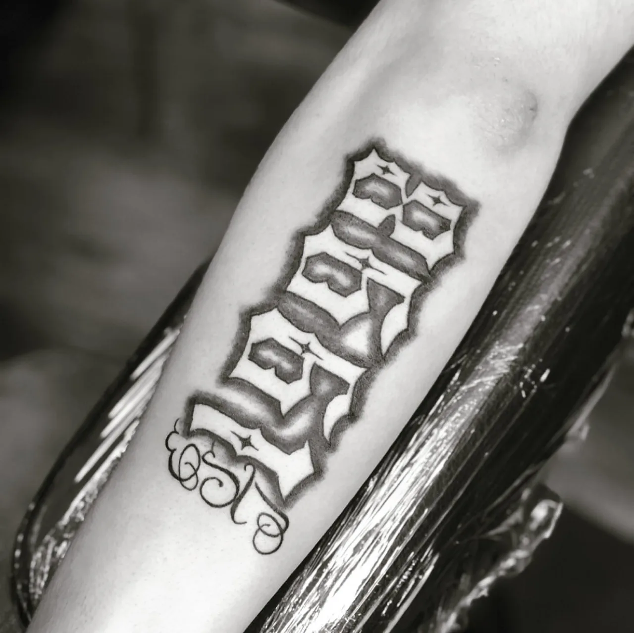 Lettering black and grey tattoo on the forearm by Charlie Soto