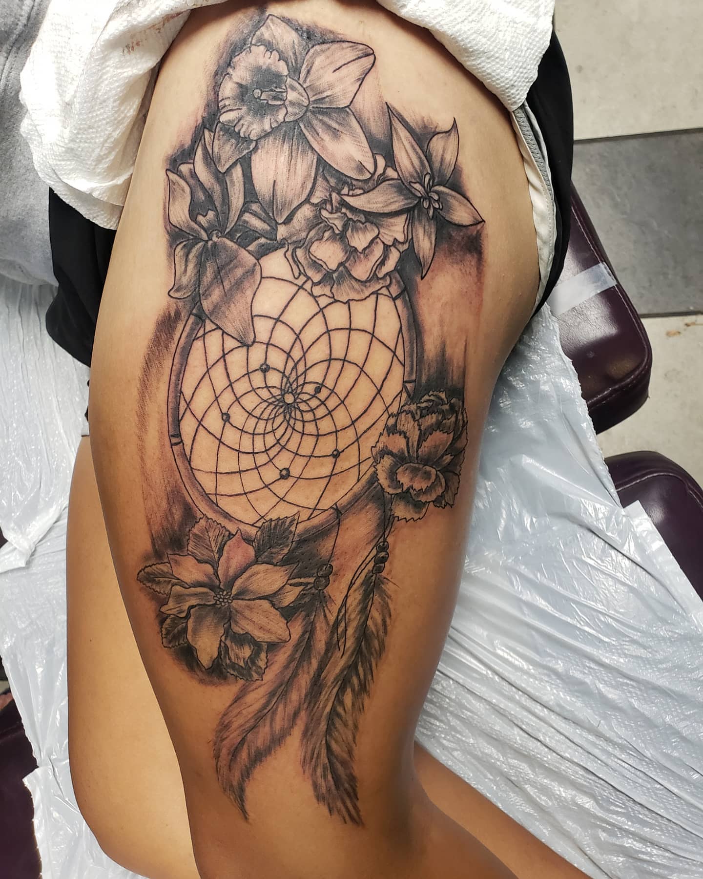 Dreamcatcher and flowers realism tattoo on the thigh by Glen Wallis
