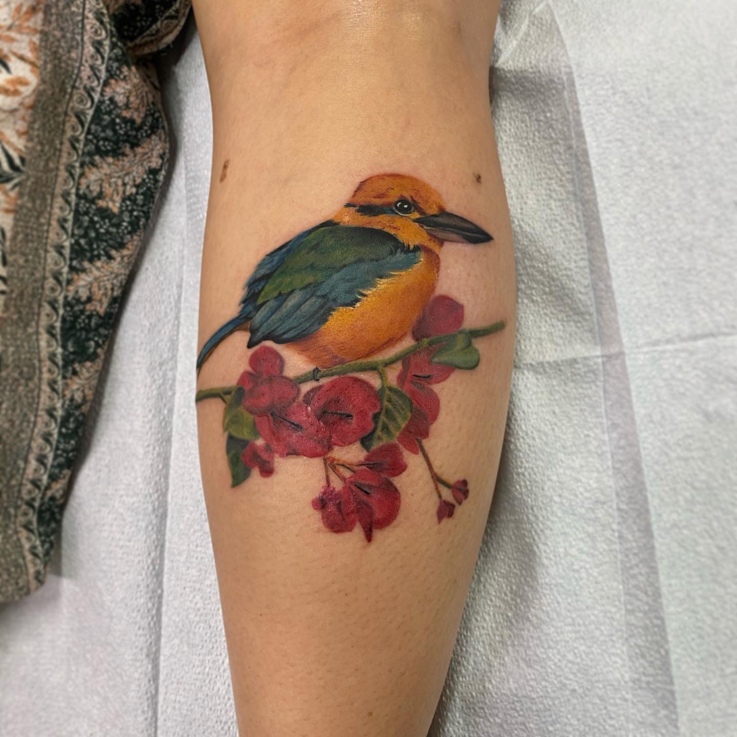 Kingfisher and blossoms realism tattoo on the forearm by Junior Nunez