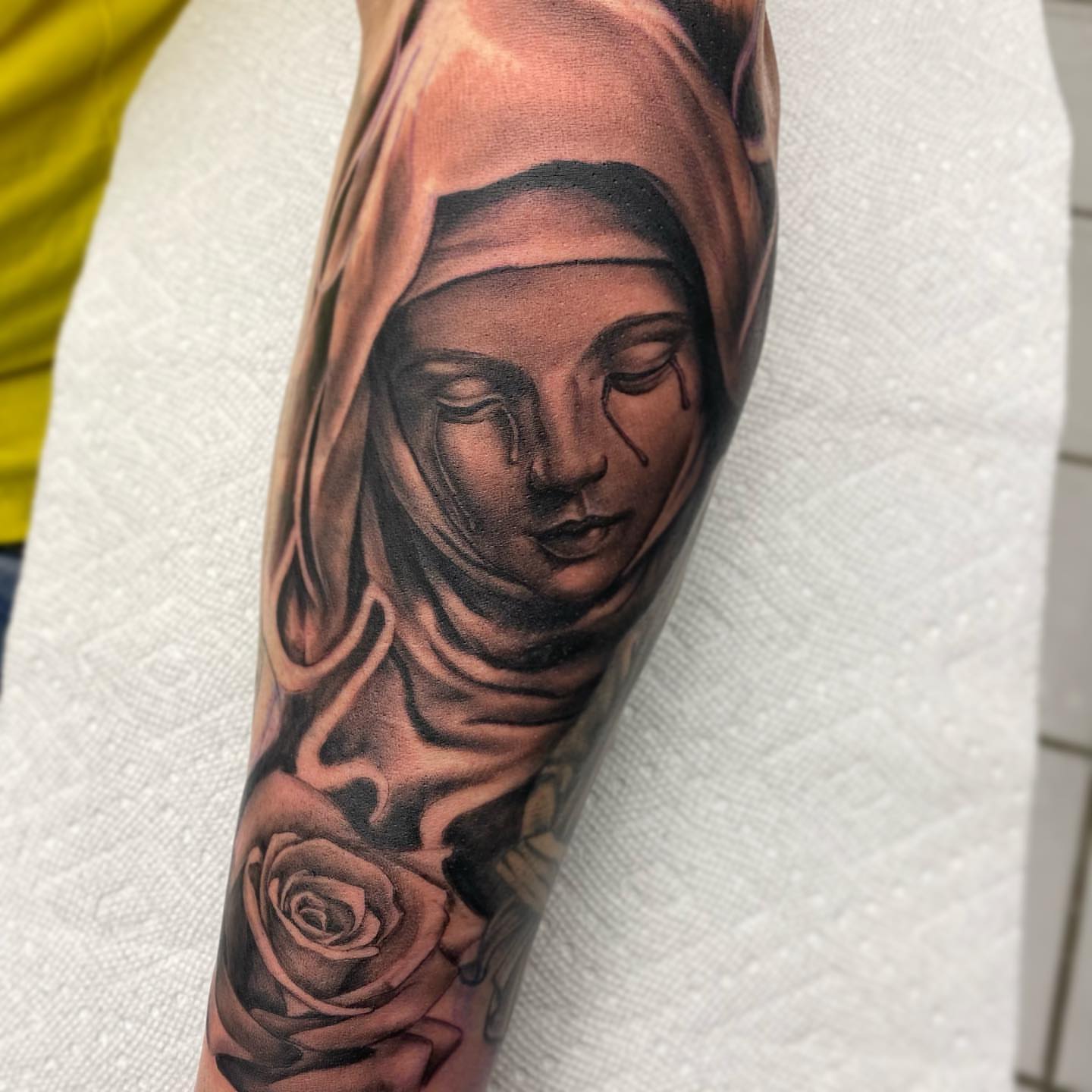 Religious figure with roses realism tattoo on the forearm by mike hudson