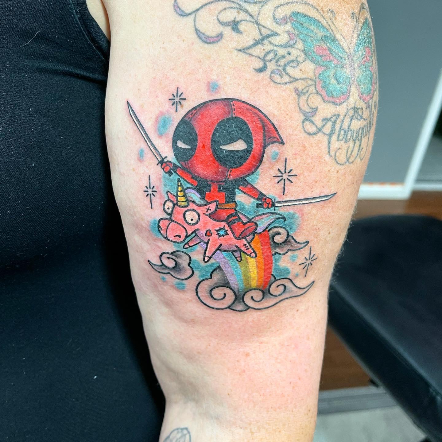 Chibi Deadpool riding a unicorn new school tattoo on the forearm by Zack Havoc
