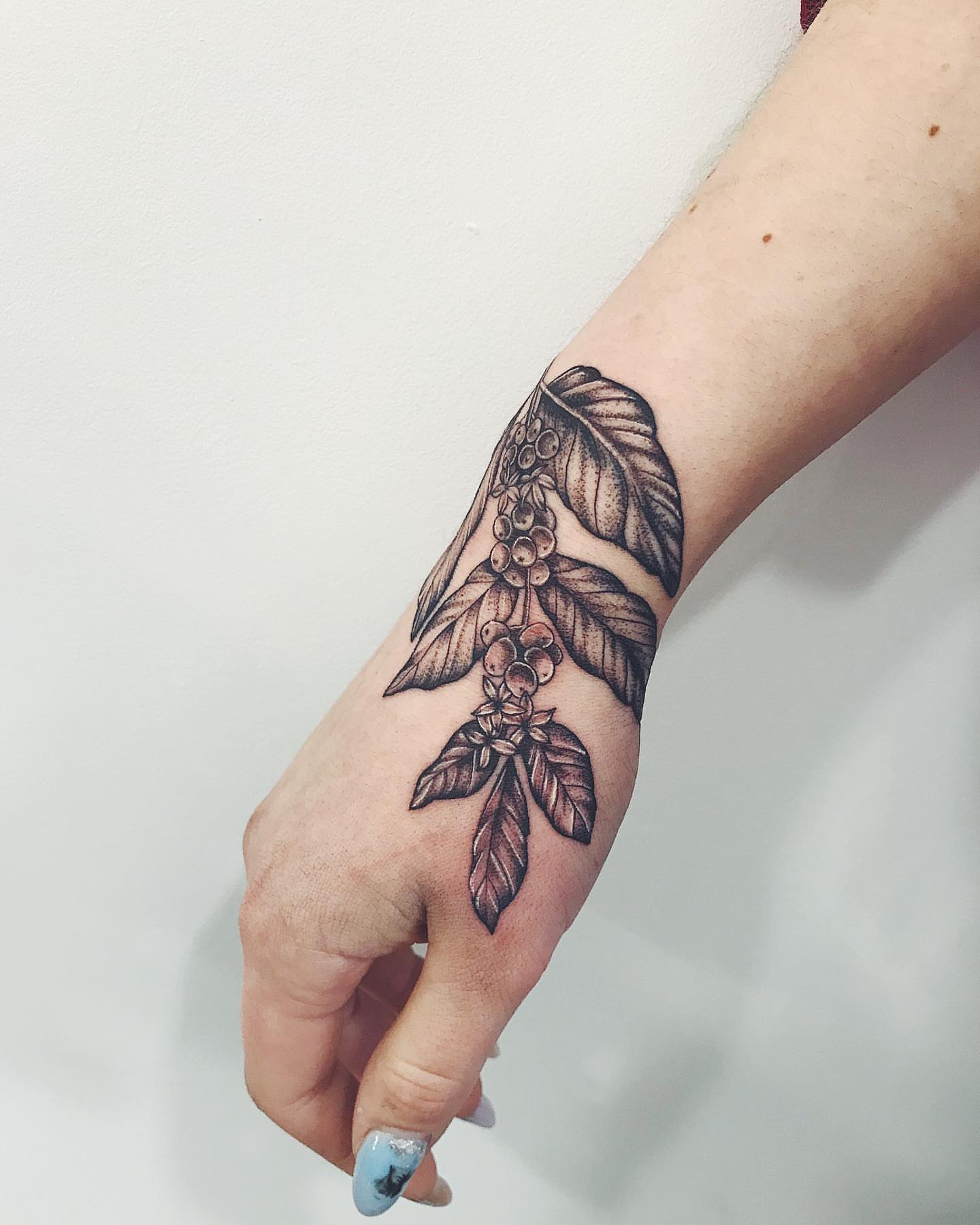 Coffee beans and leaves black and grey tattoo on the hand by Annie Overchuk