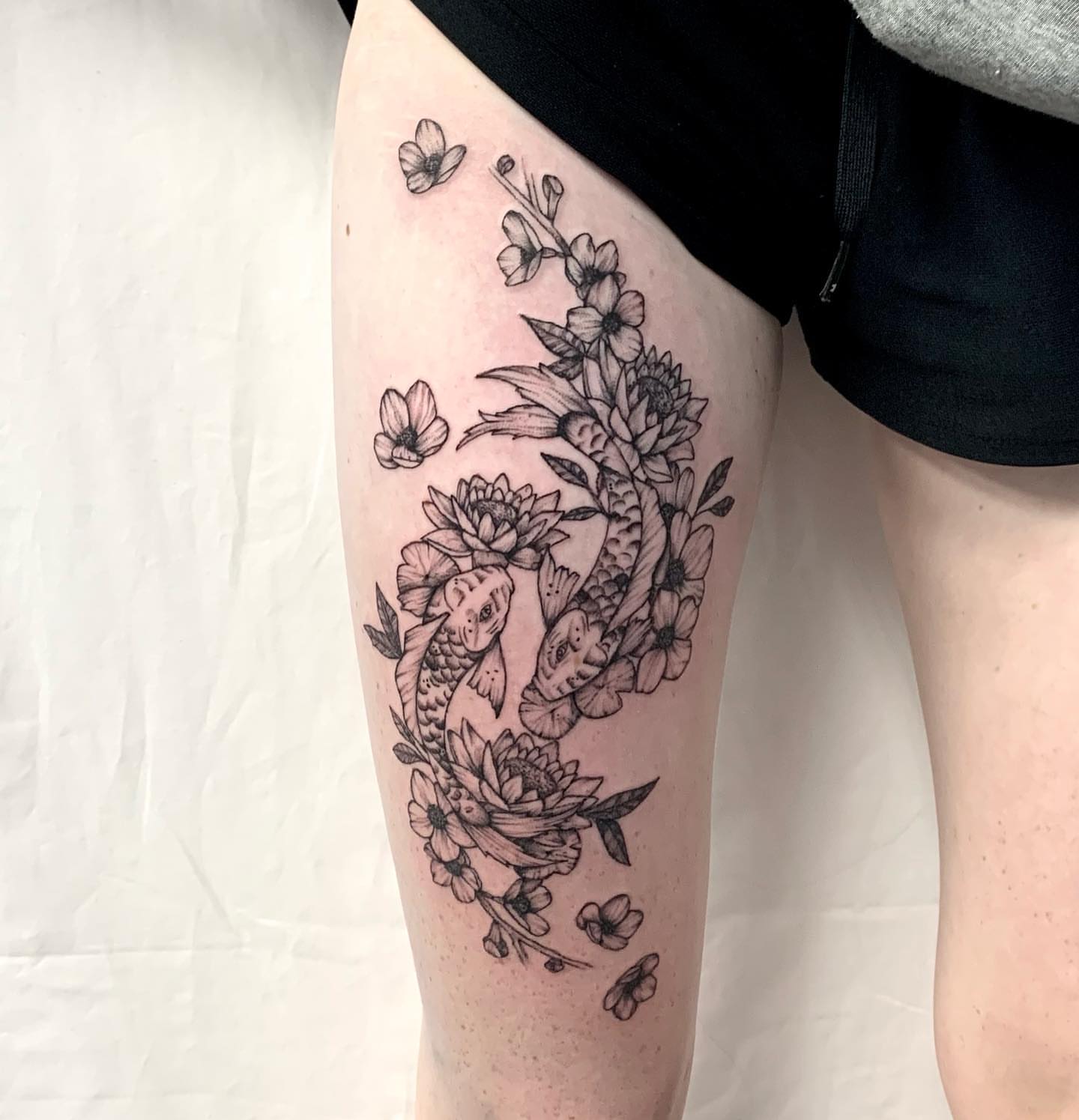Koi fish and flowers black and grey tattoo on the thigh by Megan McKee Tattoo Artist