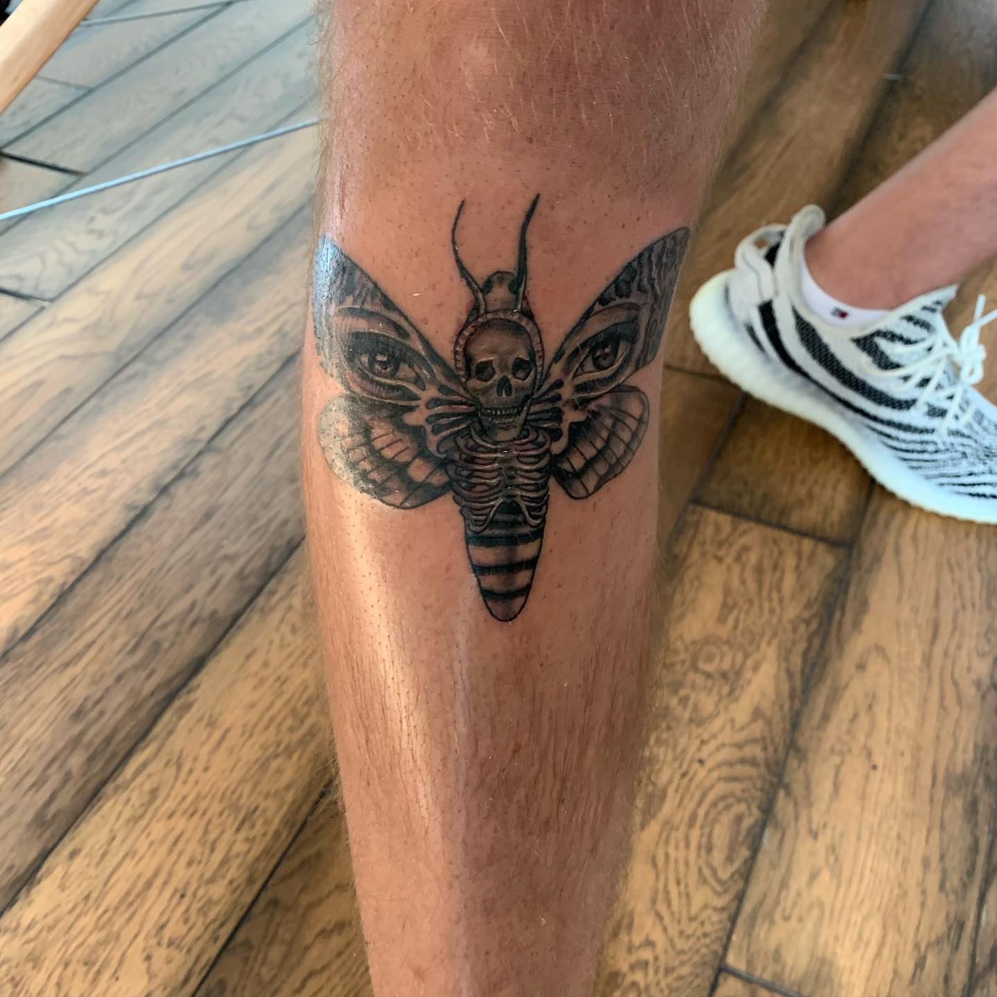 Moth with skull head black and grey tattoo on the leg by Leo Torres