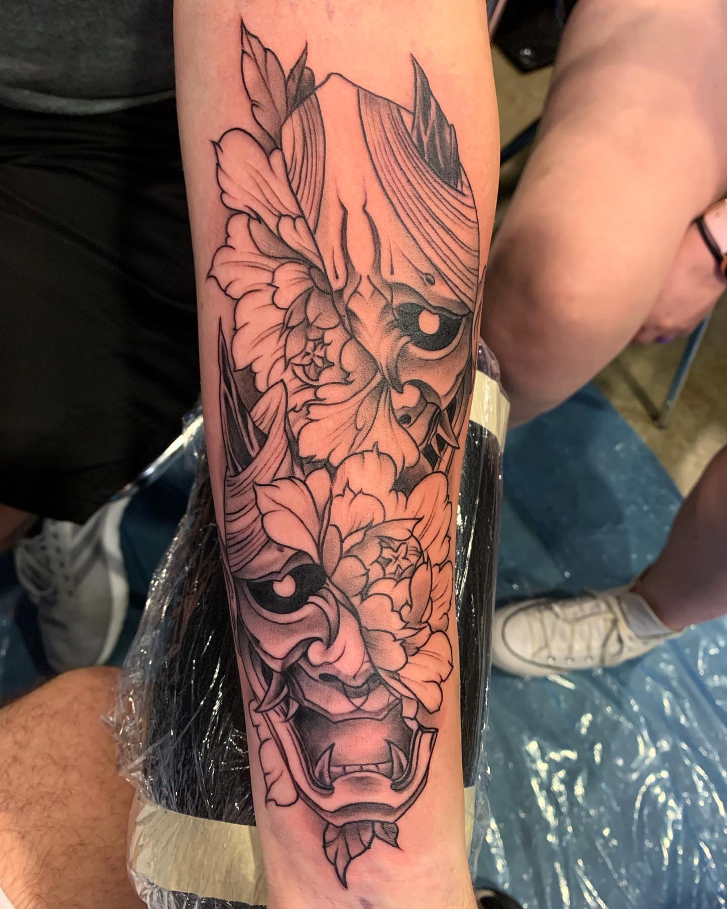 Mask and flowers realism tattoo on the forearm by Trevor Sibary