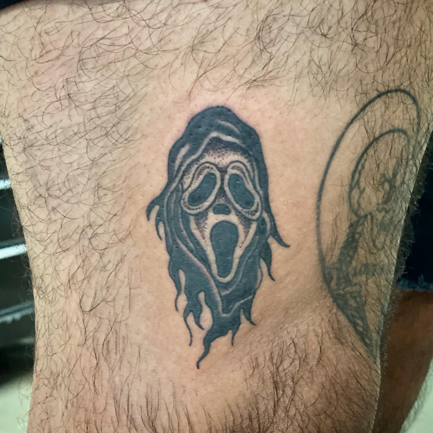 Ghost mask black and grey tattoo on the thigh by Erin Stephens