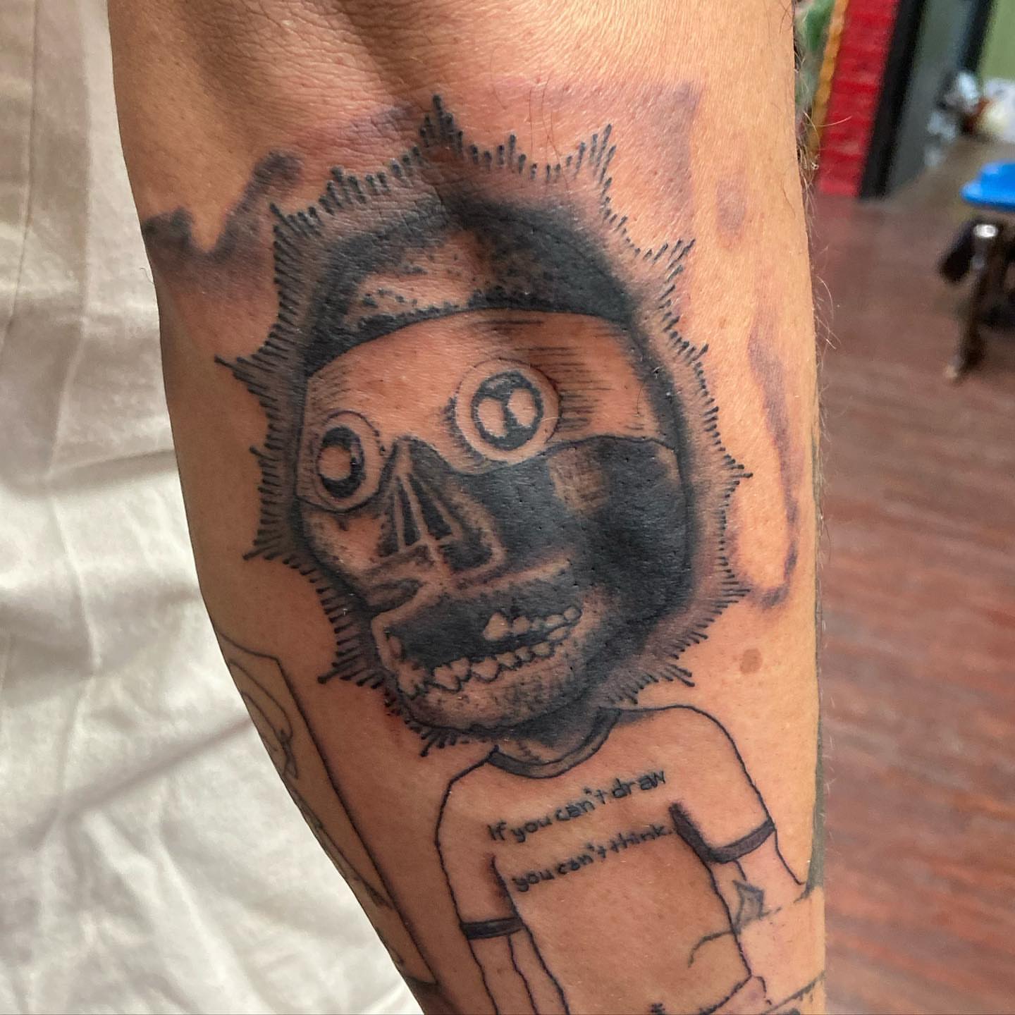 Skull with text black and grey tattoo on the forearm by Chuck House