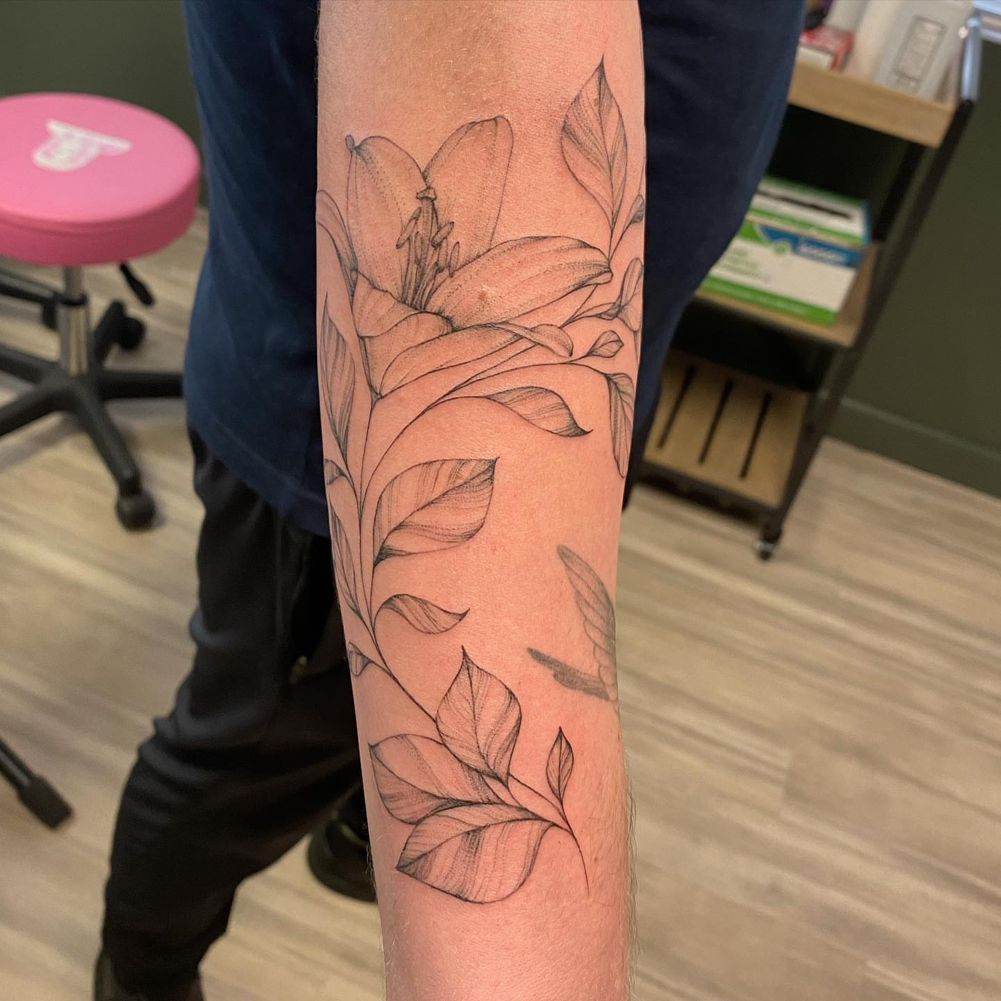 Lily and leaves black and grey tattoo on the forearm by Emily Conner