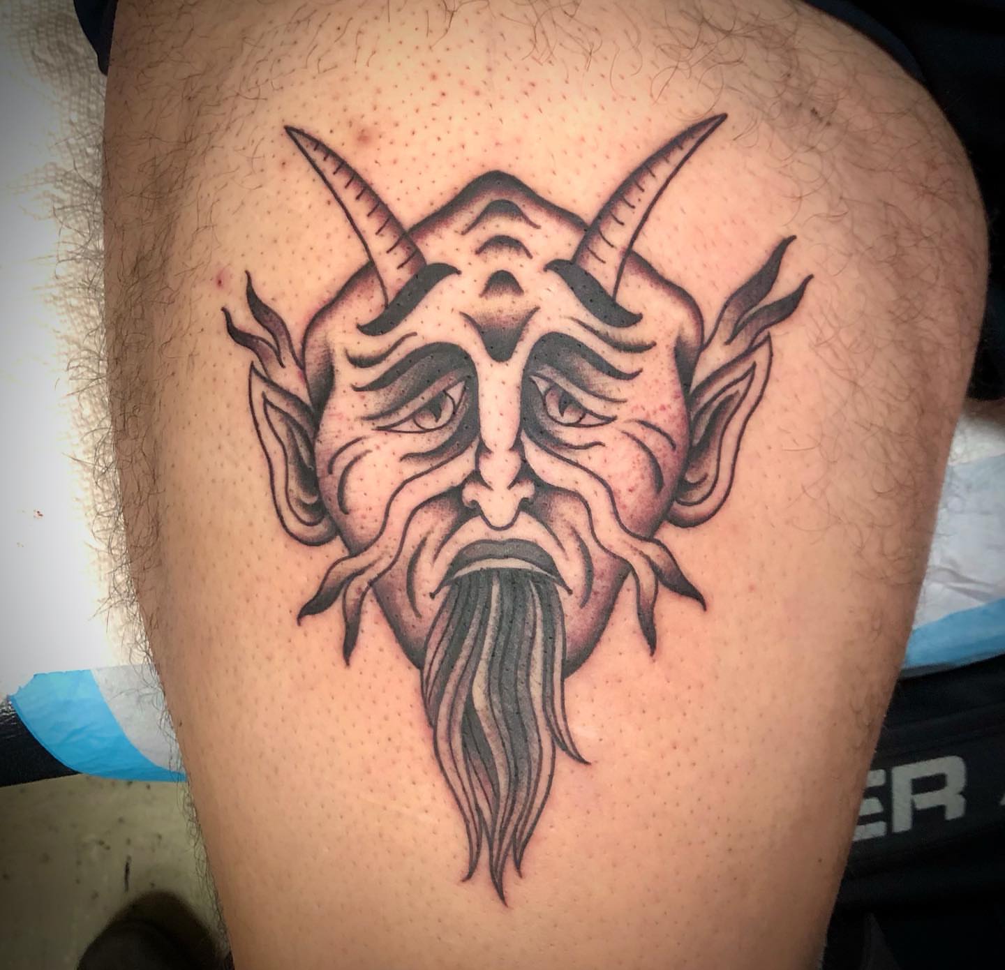 Demon mask black and grey tattoo on the thigh by Paul Trimble
