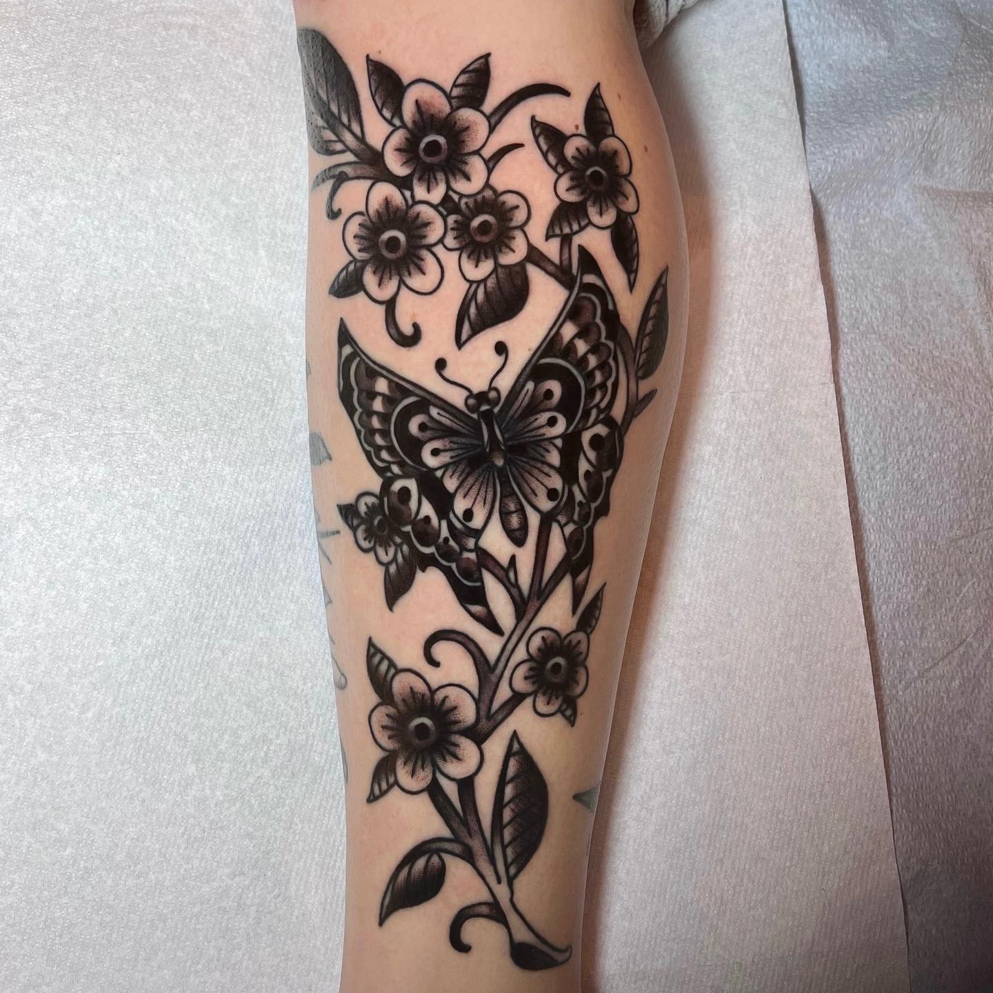 Butterfly and floral black and grey tattoo on the forearm by David Mendieta