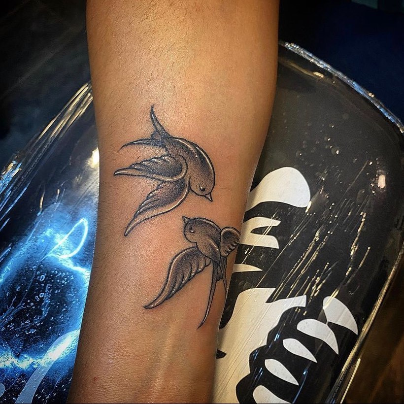 Swallows black and grey tattoo on the forearm by Visionary Tattoos
