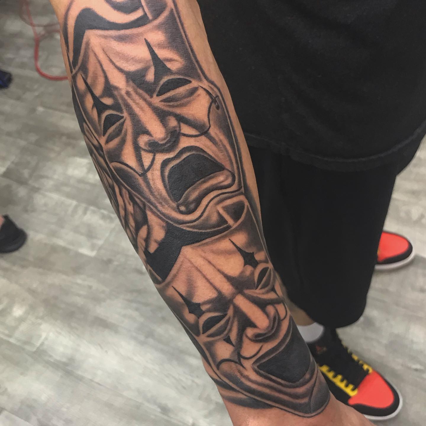 Theatrical mask realism tattoo on the forearm by James Howell
