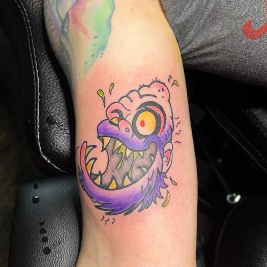 Cartoon monster face ignorant tattoo on the forearm by Wichita Tattoo