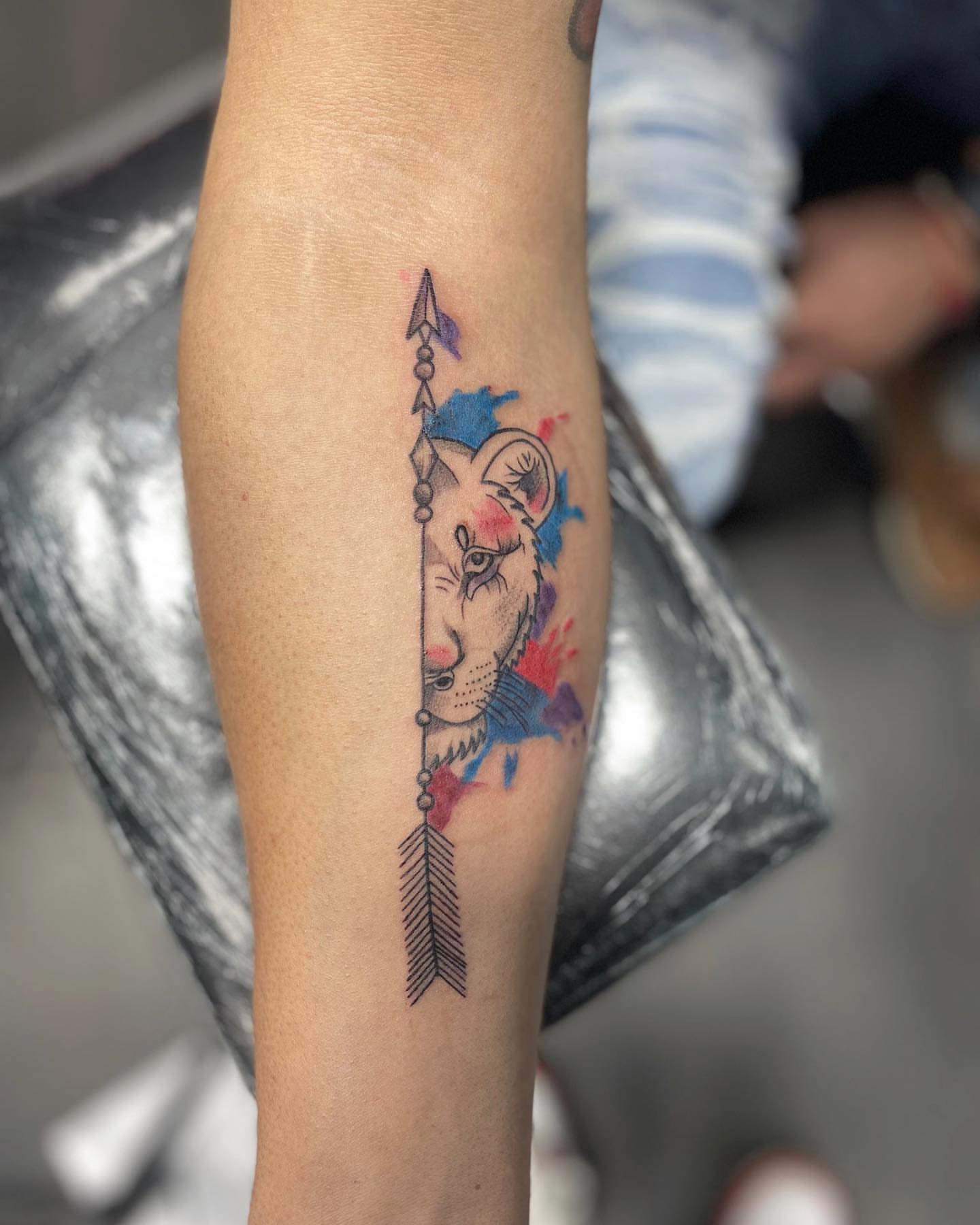 Lion head with arrow watercolor tattoo on the forearm by Alberto Ramirez