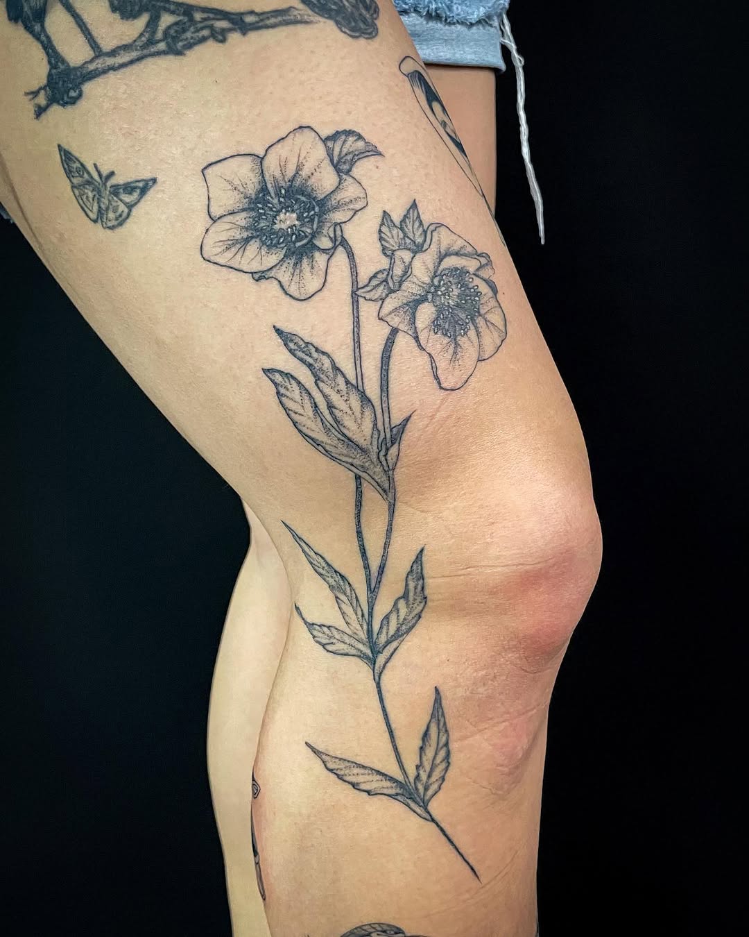 Hellebore flowers and a butterfly fine line tattoo on the thigh by Thylacine Tattoo & Art, Los Angeles, California