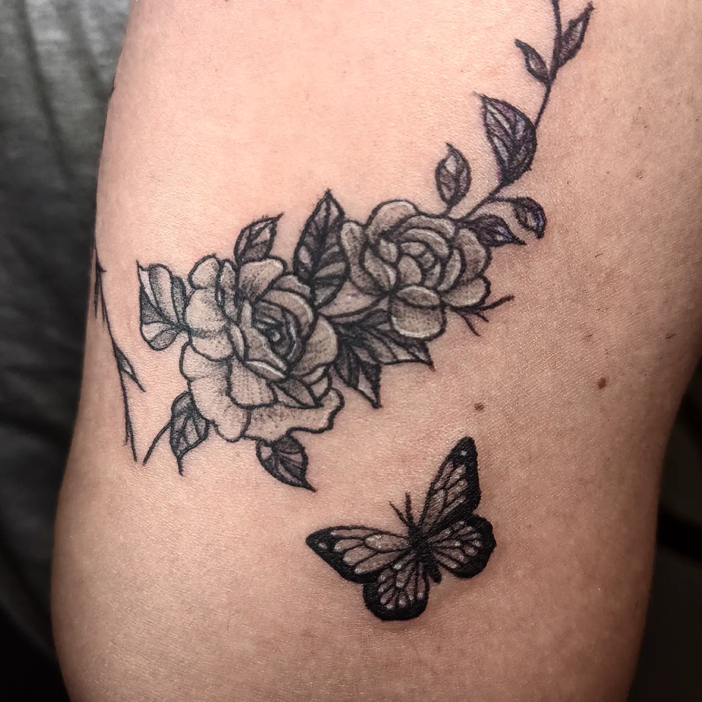 Flowers and butterfly black and grey tattoo on the thigh by Aim 🤍