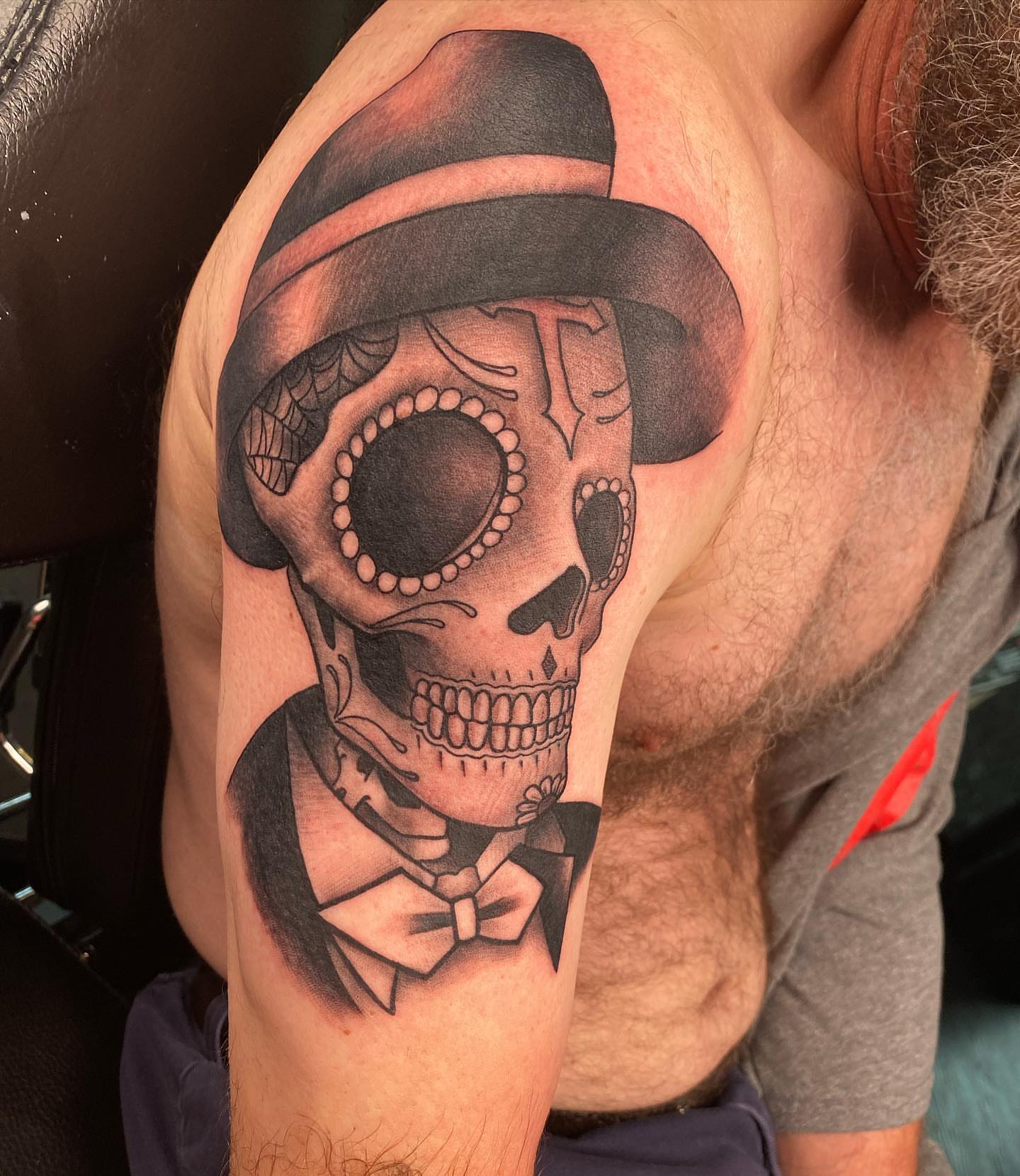 Skull wearing hat and bow tie realism tattoo on the shoulder by Seth Scott