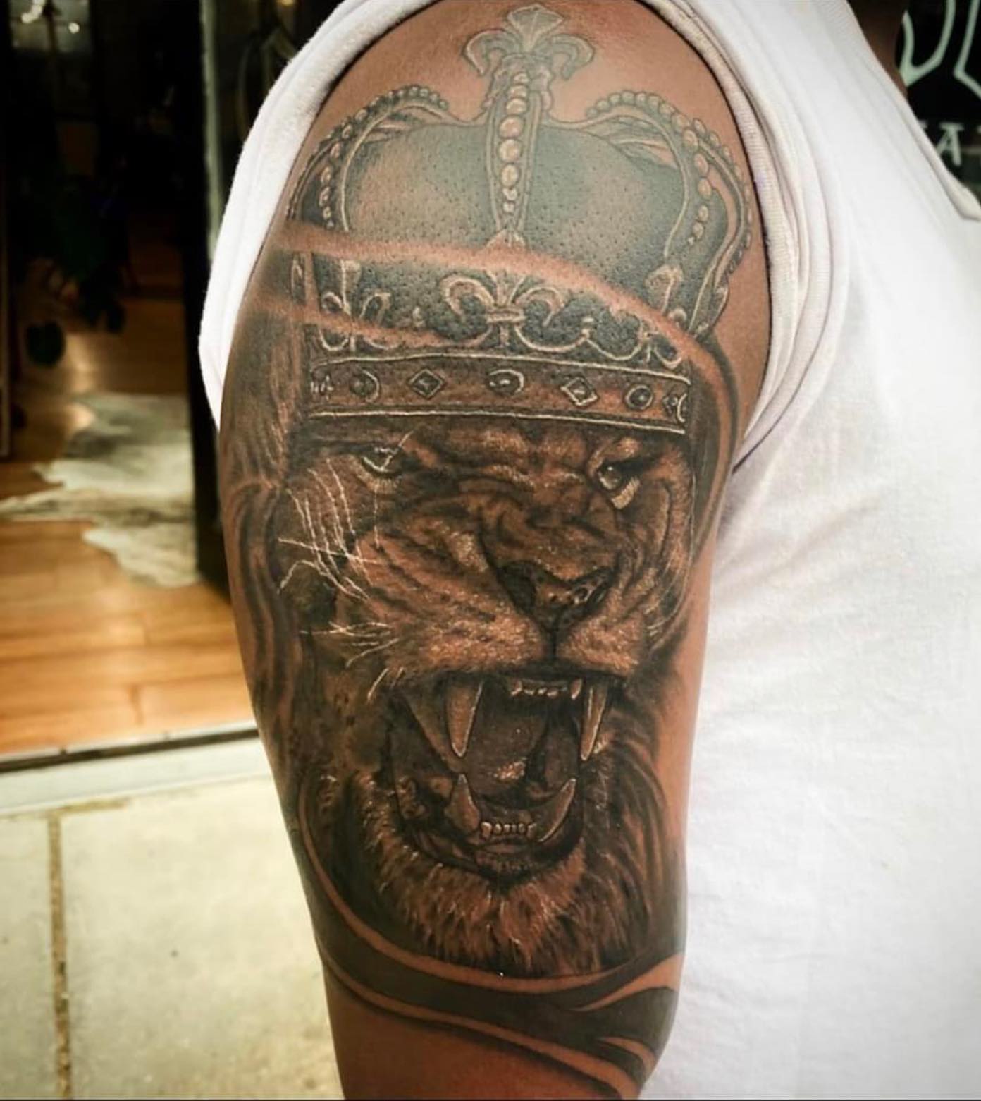 Lion with crown realism tattoo on the upper arm by Lauren Schwier