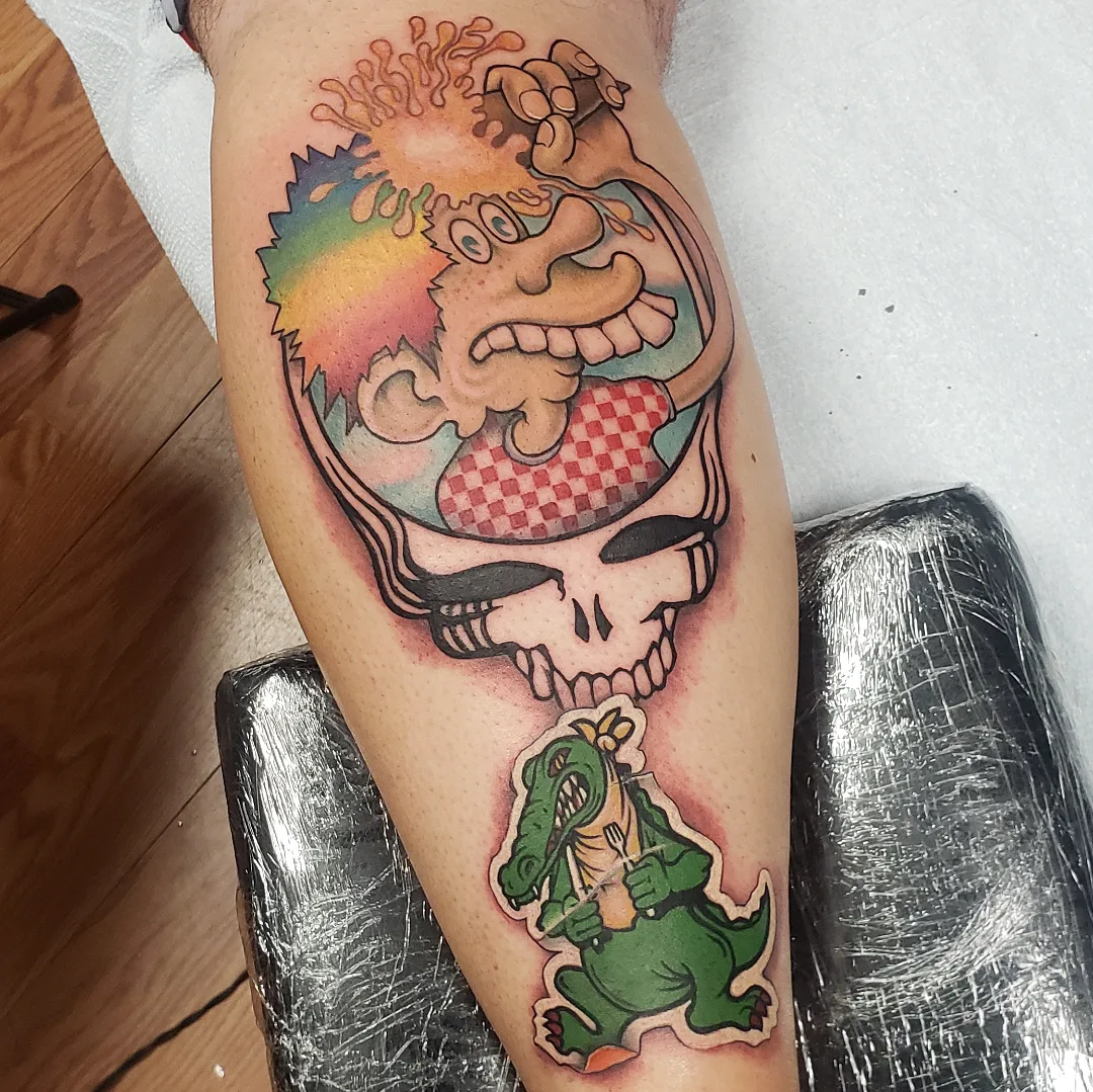 Stealie skull with dinosaur trash polka tattoo on the thigh by Don Taylor