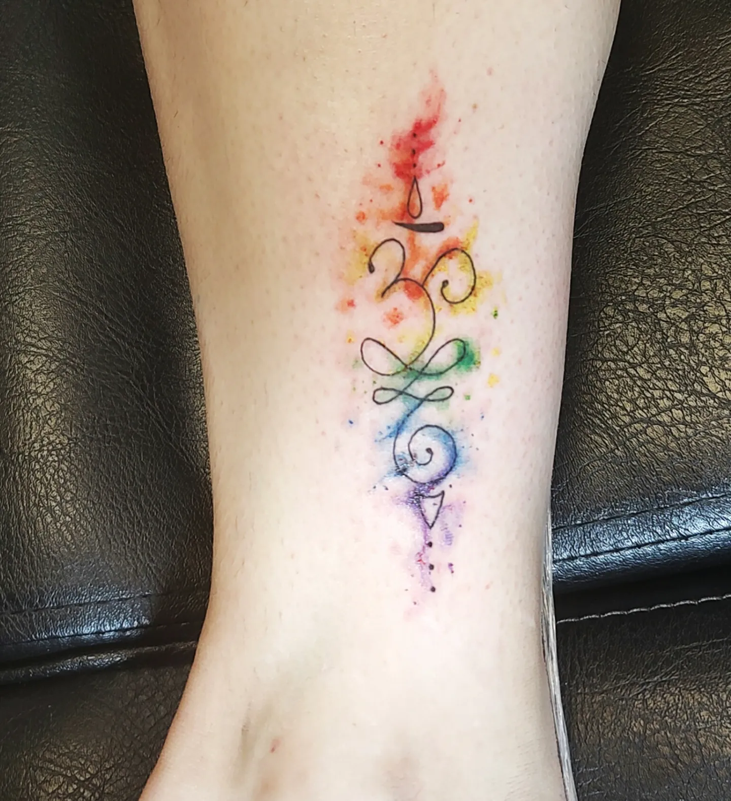 Om symbol watercolor tattoo on the calf by Madelynne