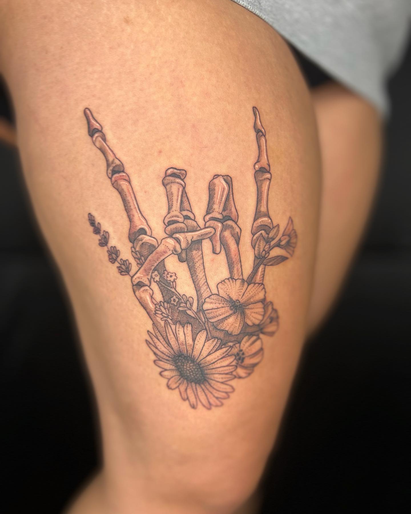 Skeleton hand with flowers black and grey tattoo on the thigh by Daphne Landry