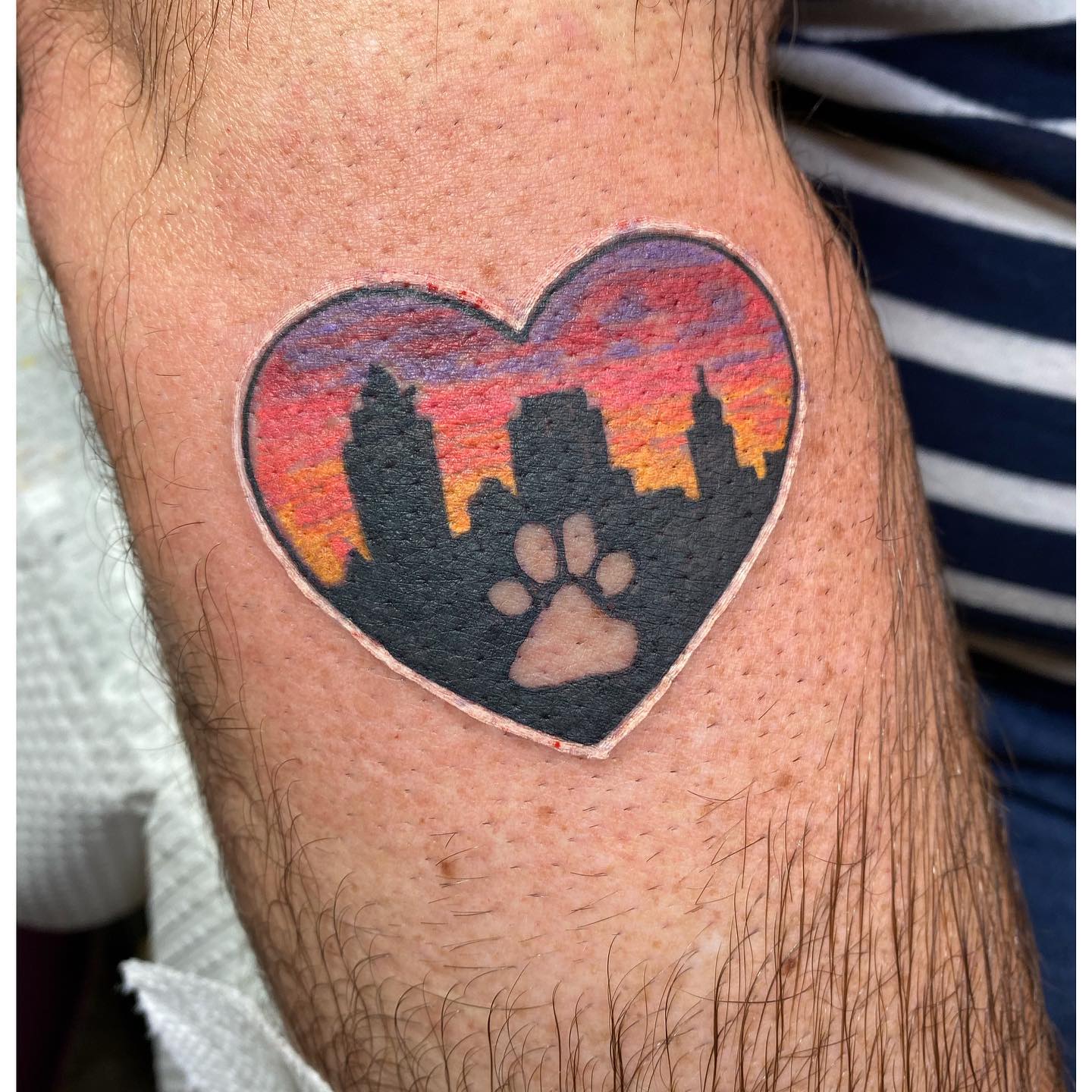 Heart with cityscape and paw print realism tattoo on the thigh by Sally Darling