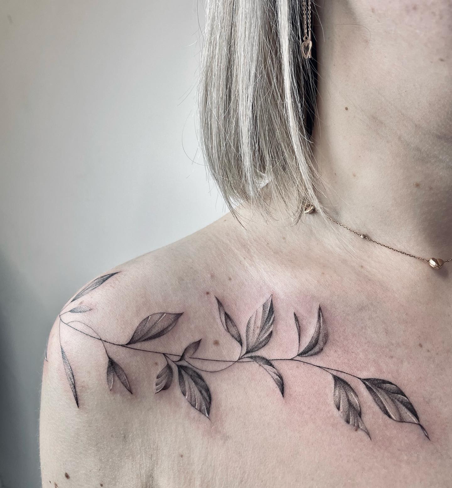 Branch with leaves black and grey tattoo on the shoulder by Annie Overchuk