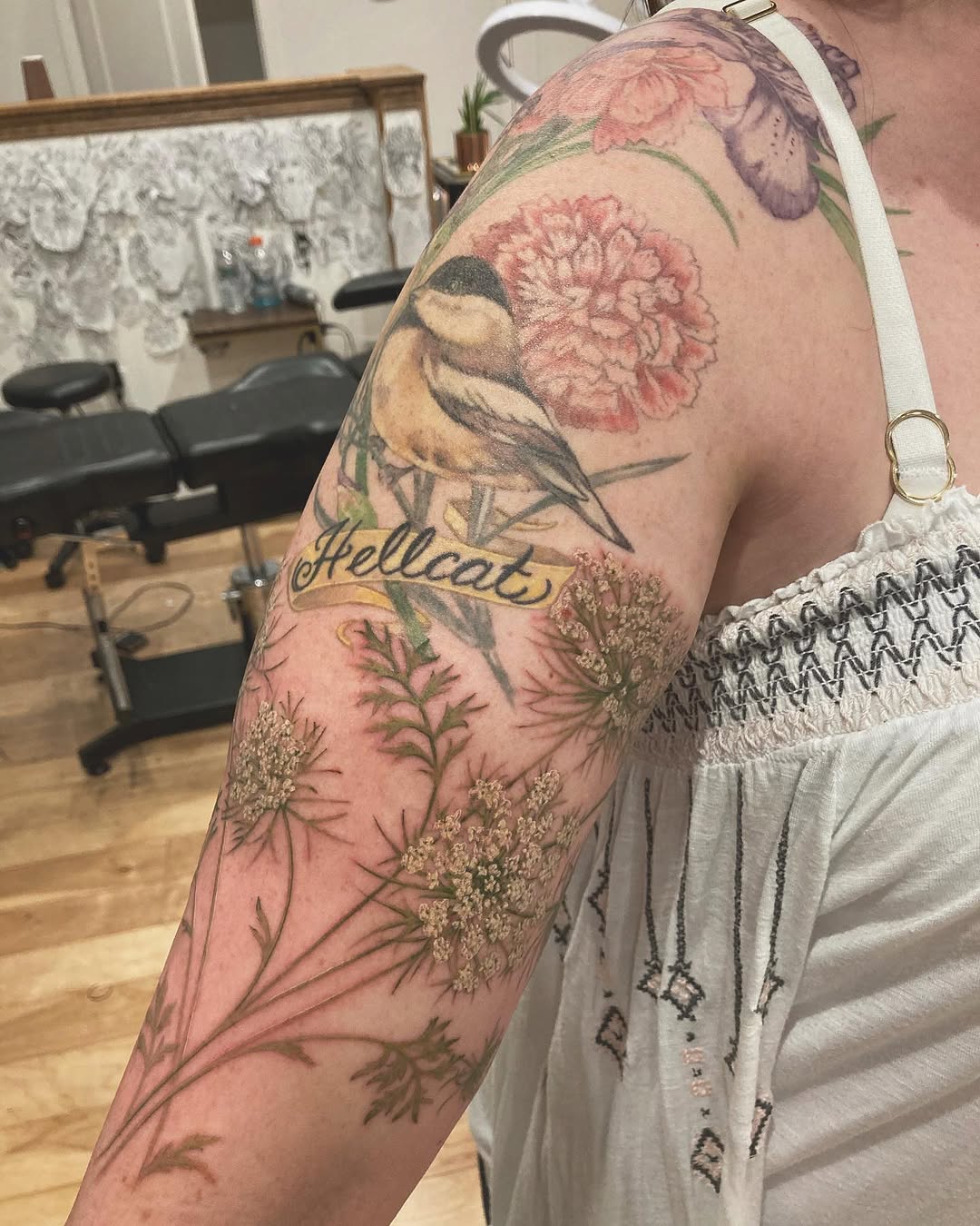 Bird and flowers with banner fine line tattoo on the upper arm by Rachel Walker