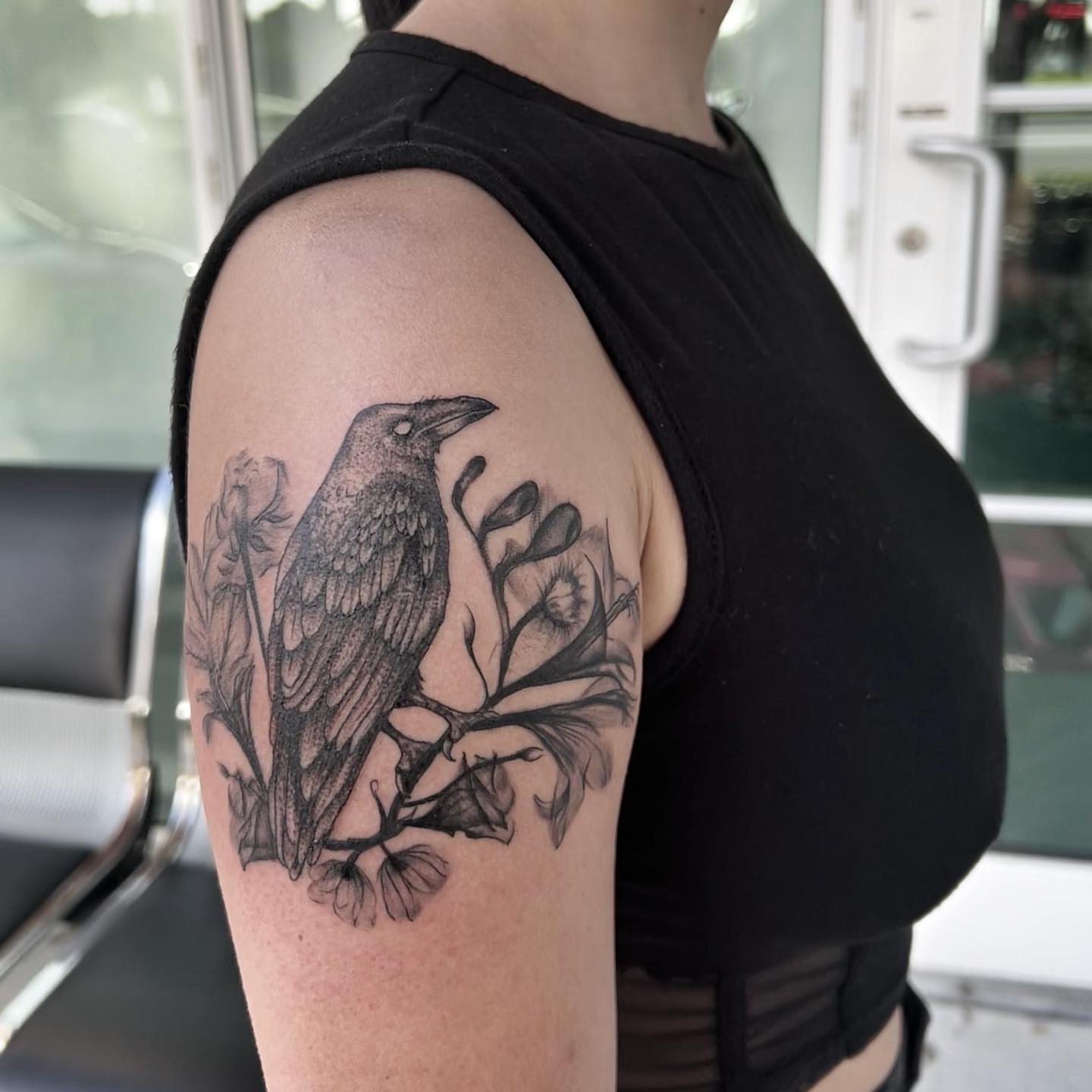Crow and flora realism tattoo on the upper arm by Syd Cheyenne