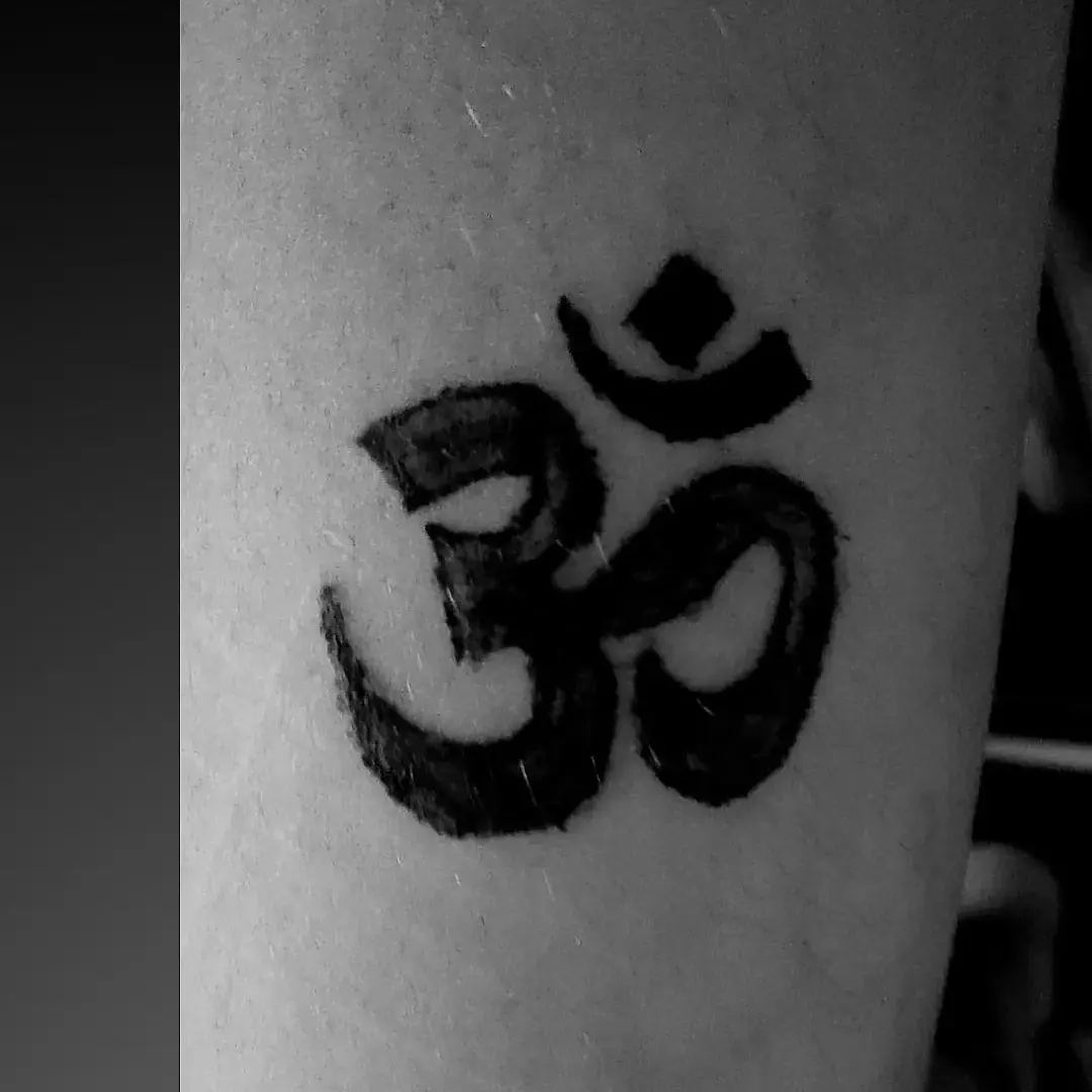 Om symbol black and grey tattoo on the forearm by Tatuadora & Piercer