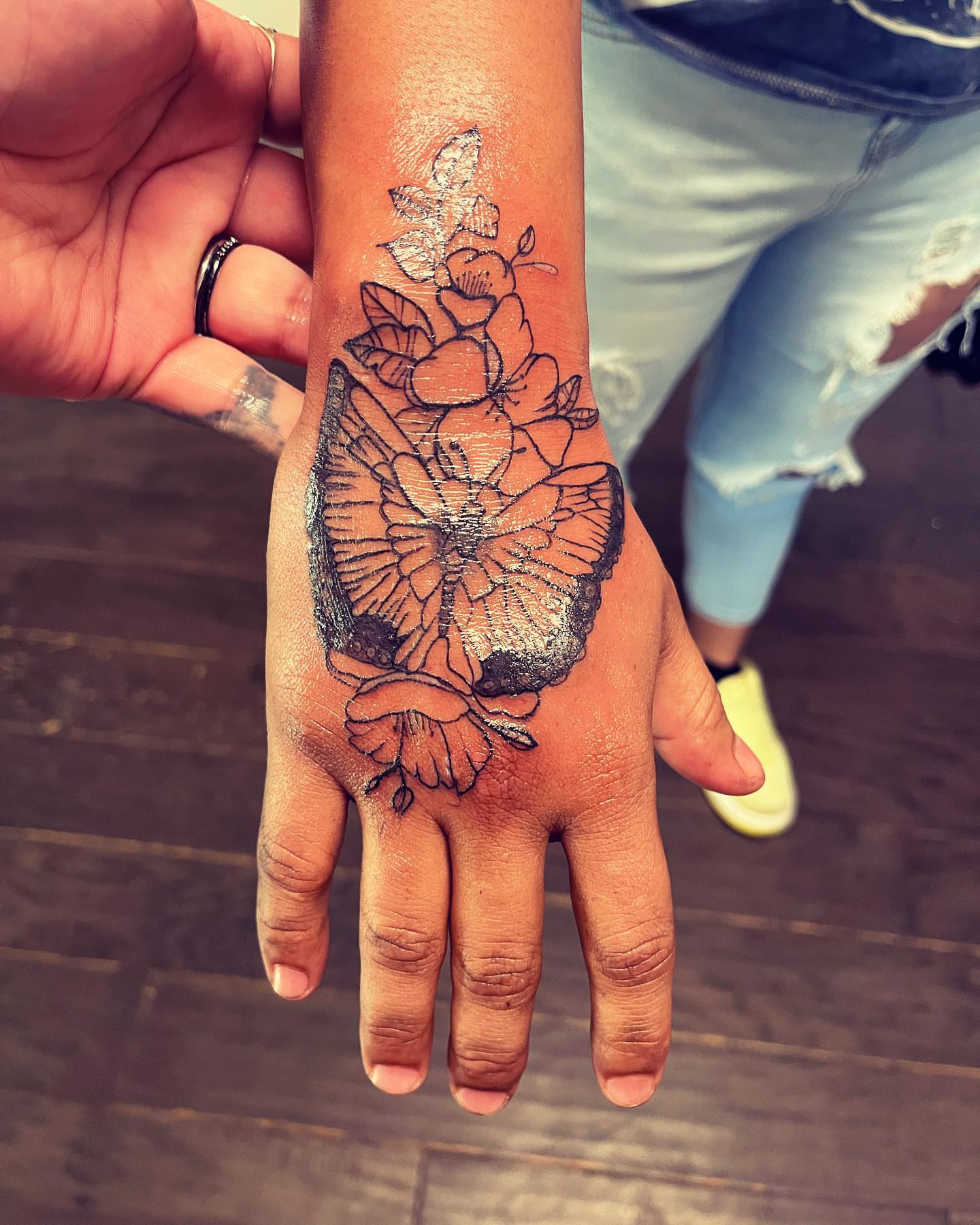 Butterfly and flowers black and grey tattoo on the hand by Anna DeLuna