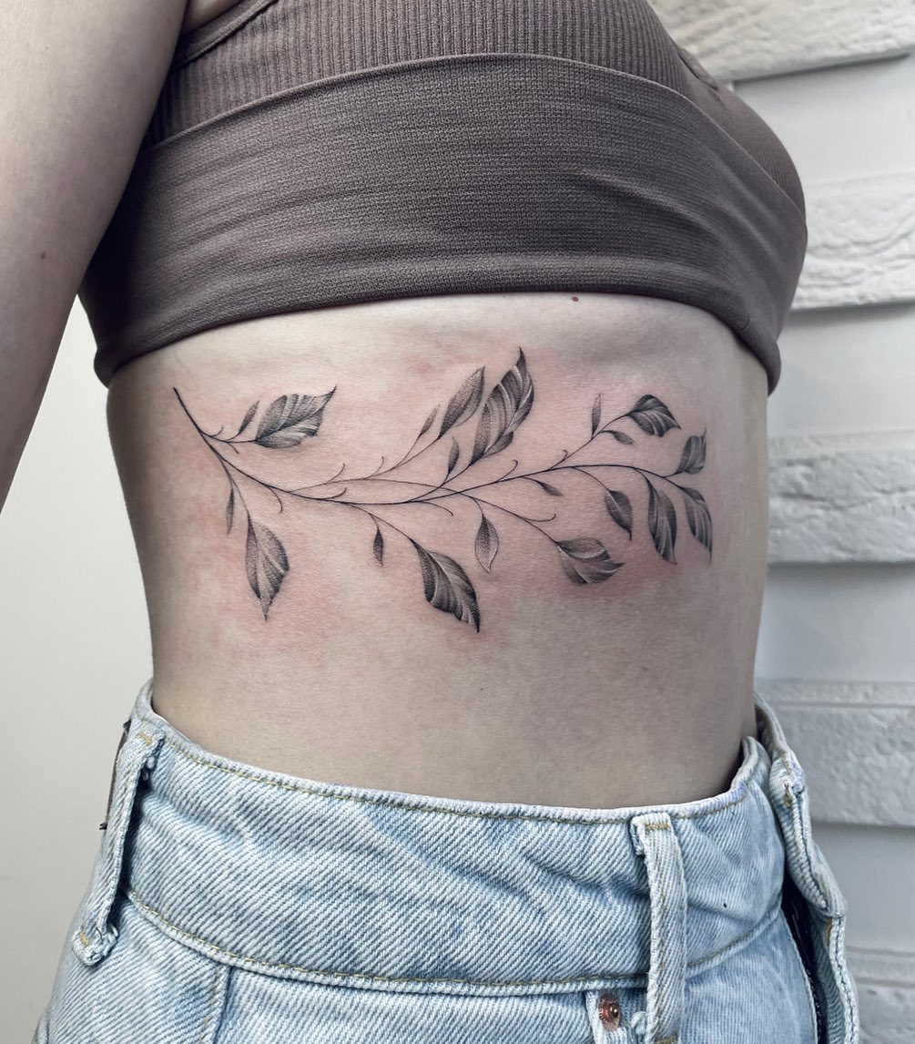 Branch with leaves black and grey tattoo on the ribs by Annie Overchuk