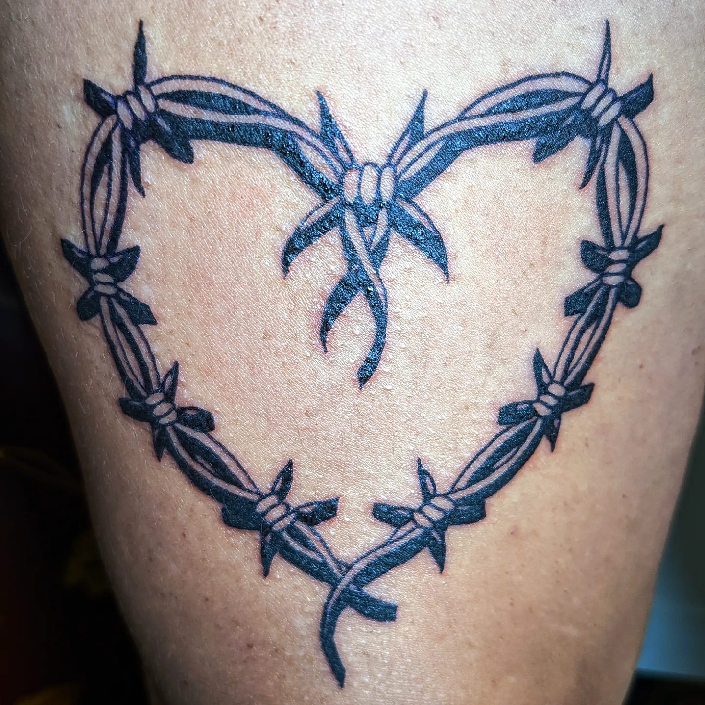 Barbed wire heart black and grey tattoo on the thigh by Aim 🤍
