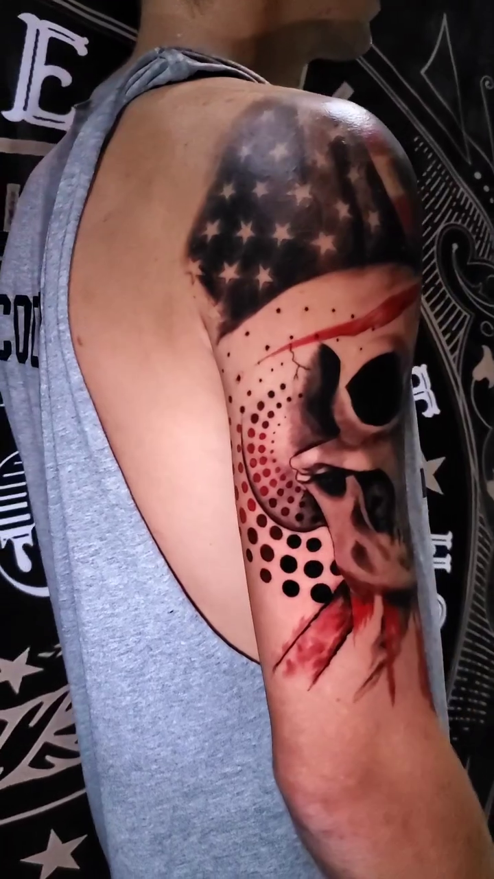 Skull with American flag and blood realism tattoo on the upper arm by BoogaInk
