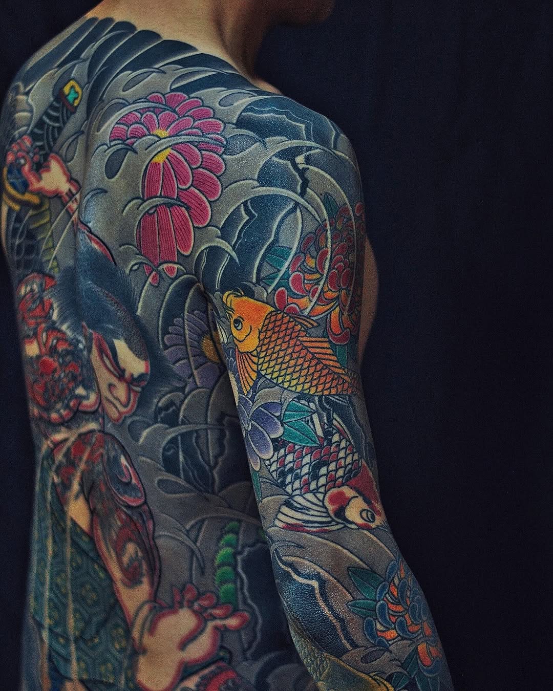 Koi fish and flowers Japanese tattoo on the upper arm by Xiaojun Yin, Vancouver, British Columbia