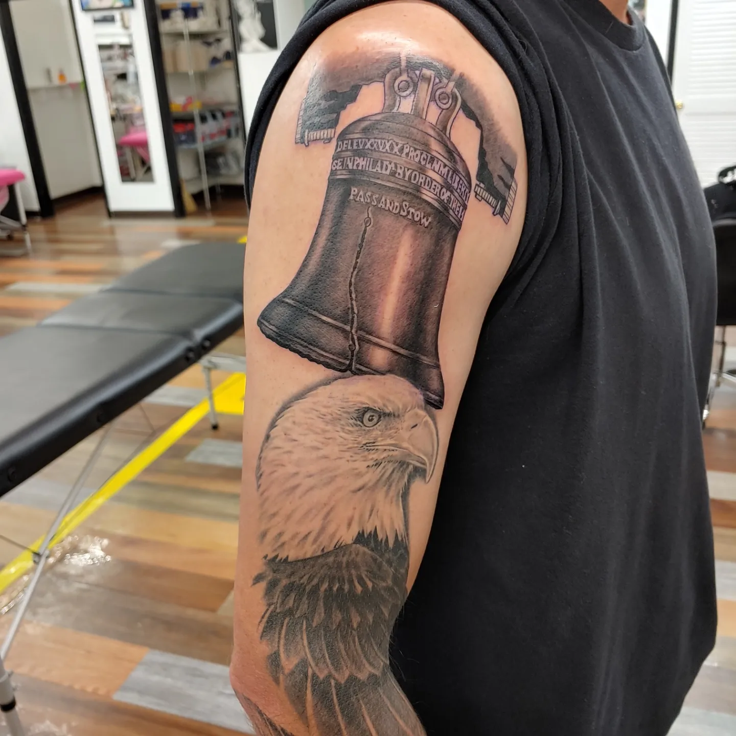 Bell and eagle realism tattoo on the upper arm by Gene Britton