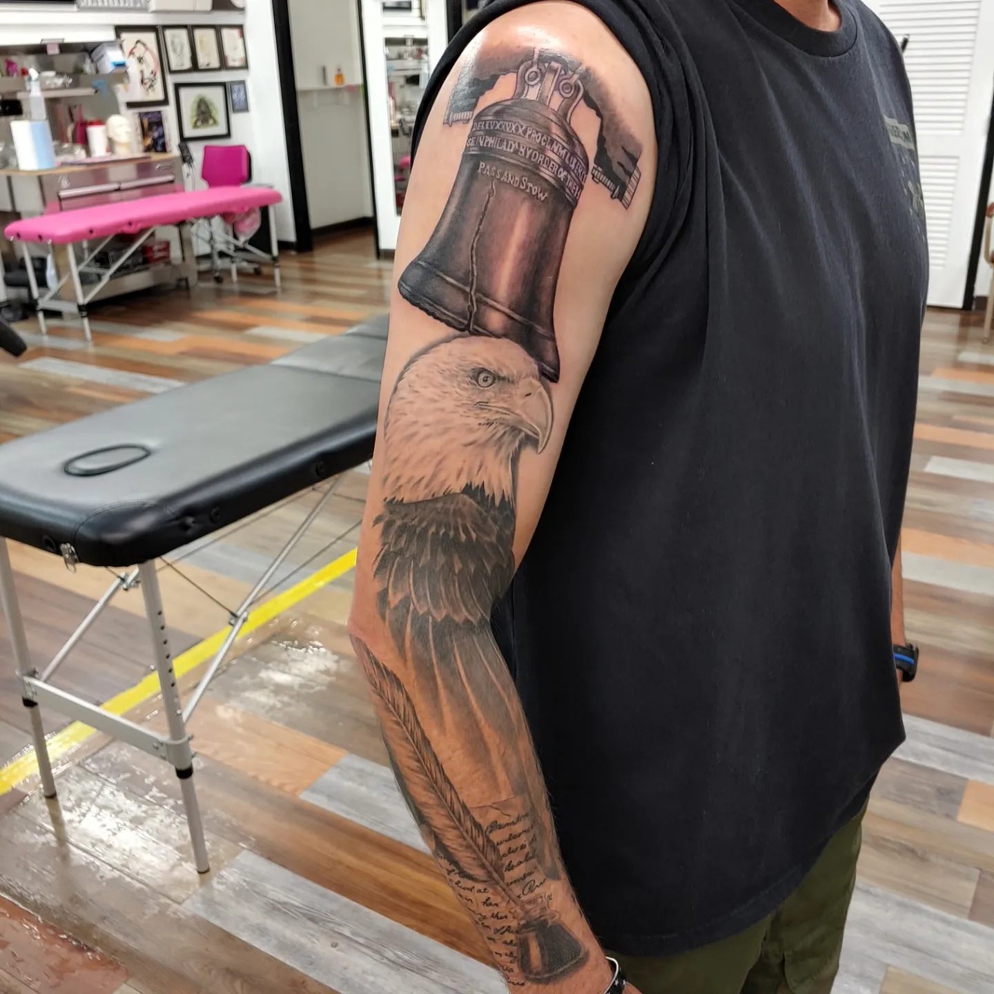 Eagle and bell realism tattoo on the upper arm by Gene Britton