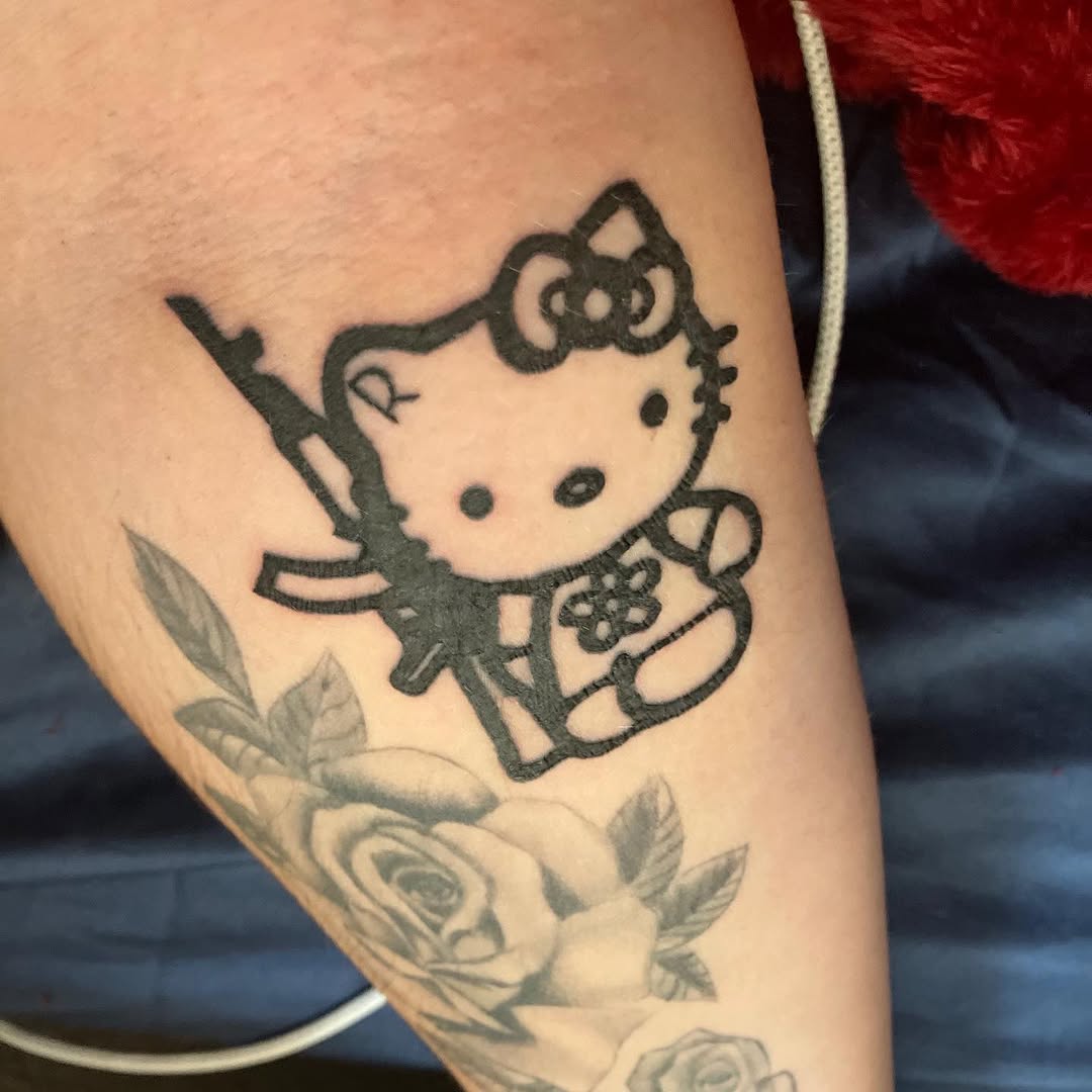 Hello Kitty with a gun new school tattoo on the forearm by Ramirez Tattooing