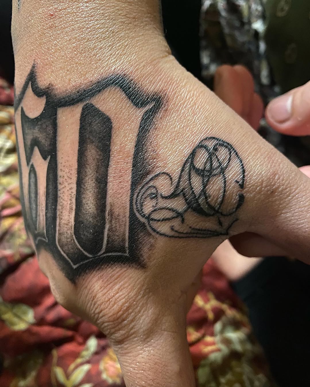 Gothic lettering with ornamental flourish Chicano tattoo on the hand by Ramirez Tattooing