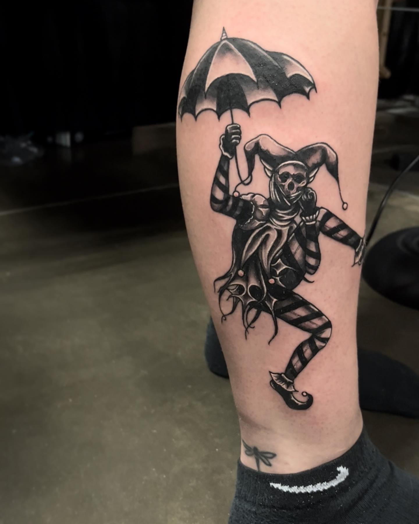 Jester with umbrella black and grey tattoo on the forearm by Myla Jane, Houston, Texas