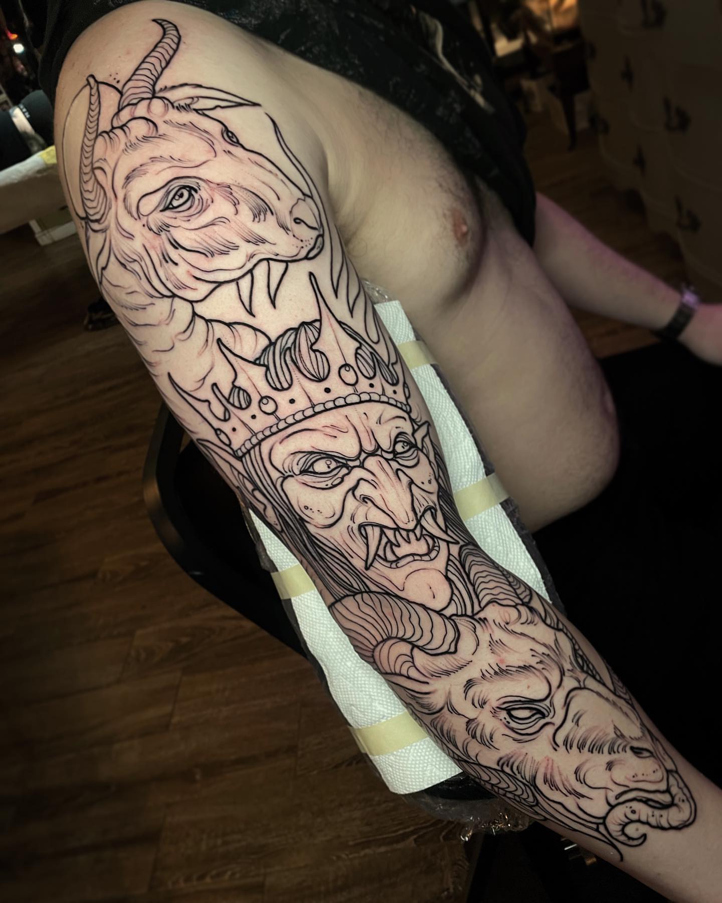 King and goat heads realism tattoo on the upper arm by Ick Abrams