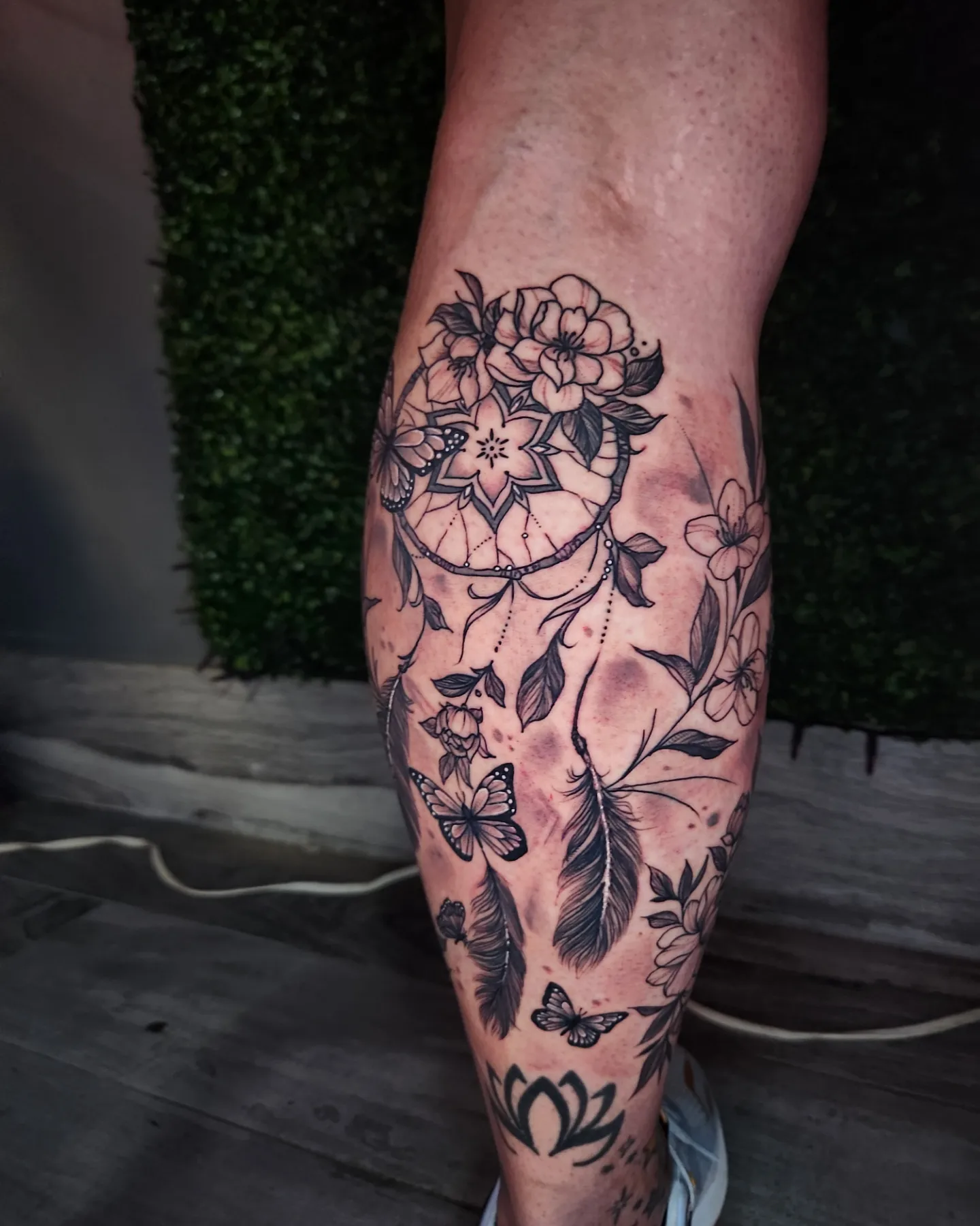 Dreamcatcher and floral black and grey tattoo on the calf by Adrian Gonzalez