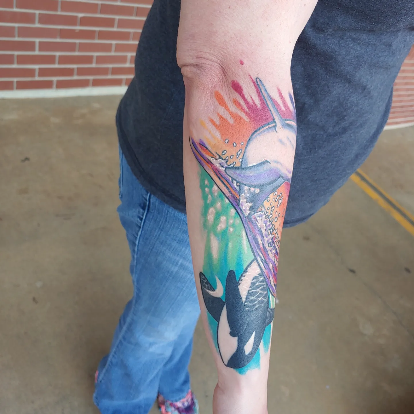 Dolphins and splash watercolor tattoo on the forearm by Gene Britton
