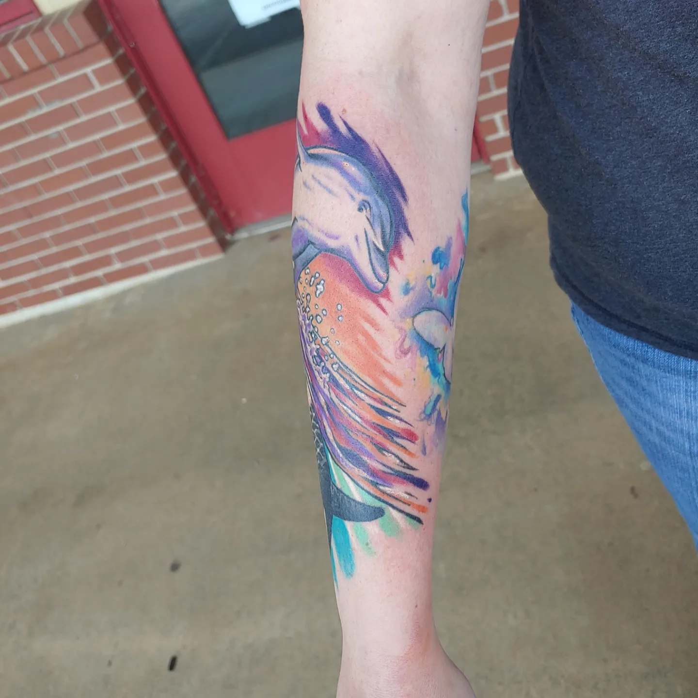 Dolphin watercolor tattoo on the forearm by Gene Britton