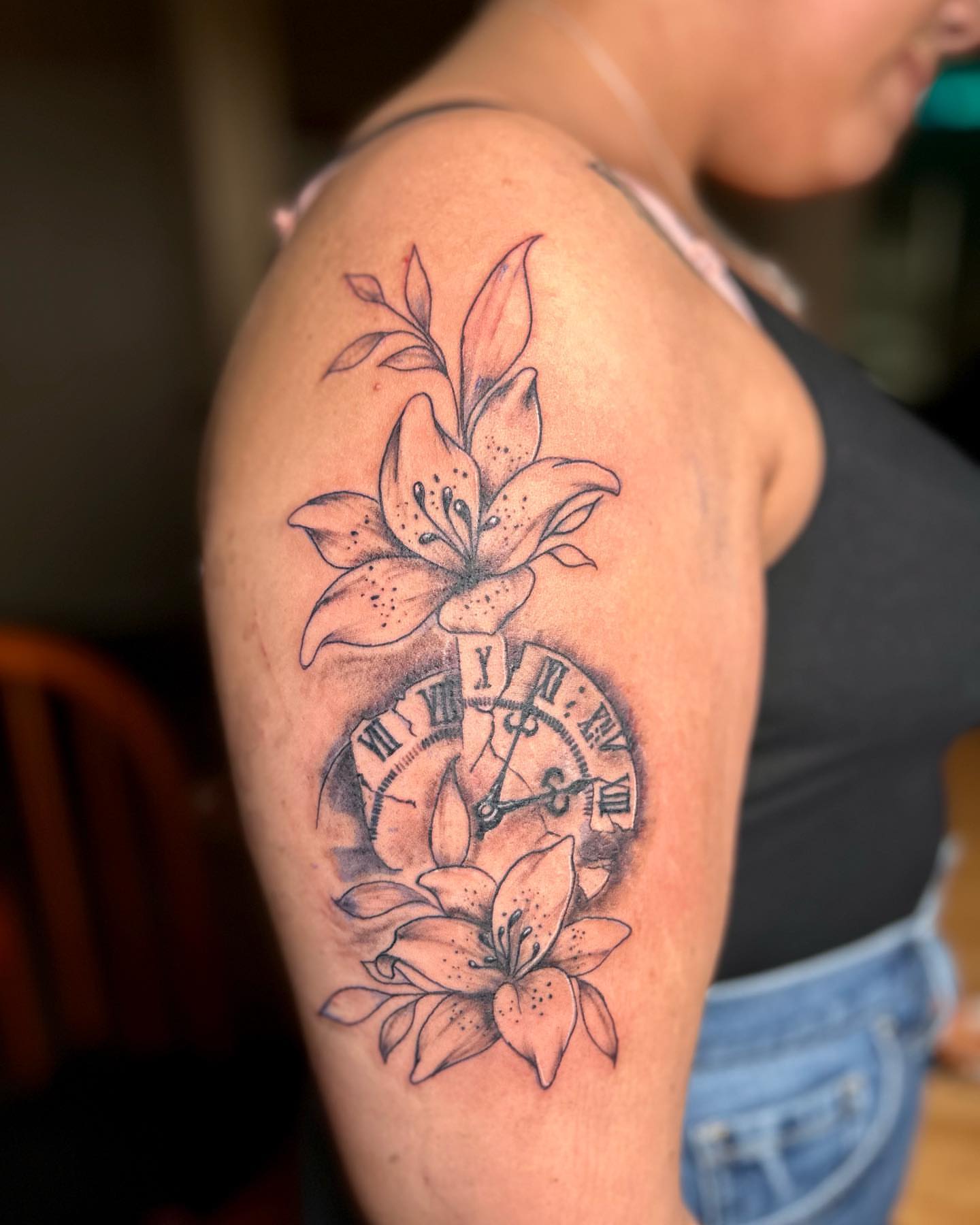Lilies and clock black and grey tattoo on the shoulder by Atl Tattoo Artist✍🏾👨🏾‍🎨