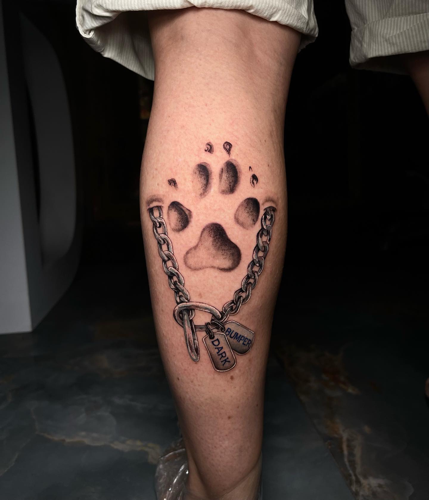Paw print with chain dotwork tattoo on the calf by Dori