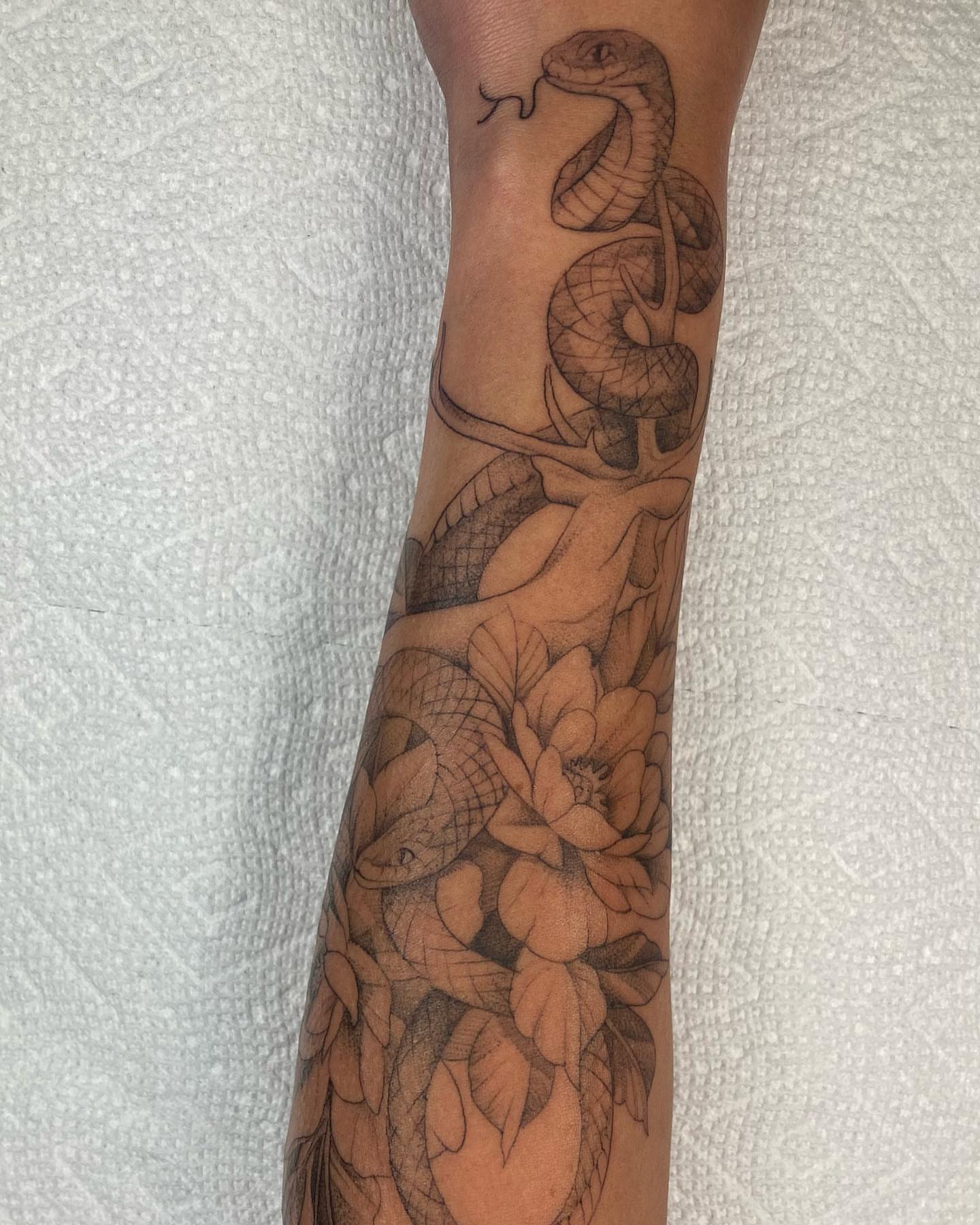 Snake and flowers black and grey tattoo on the forearm by Hali Larkin
